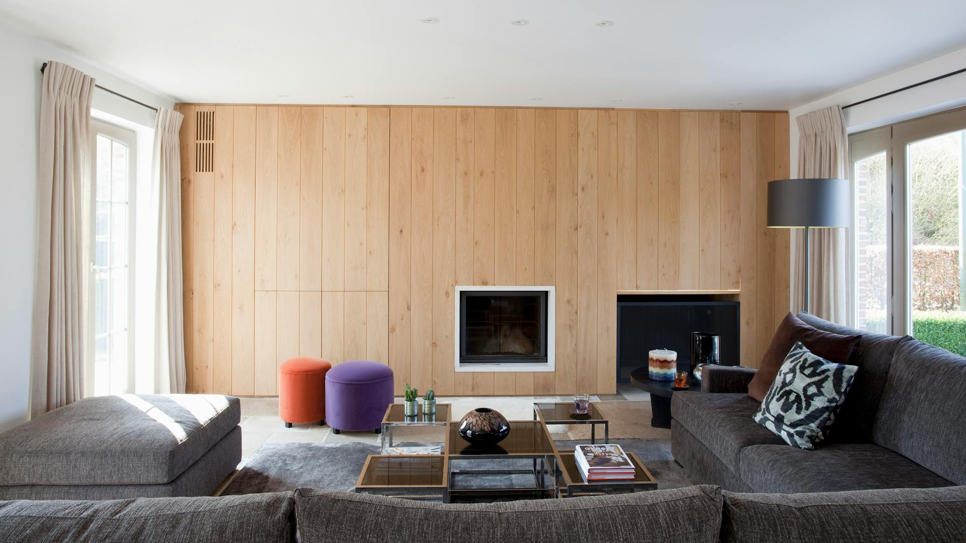 Helle Holzpaneele in einem hellen Wohnzimmer mit grauen Möbeln und Kamin.