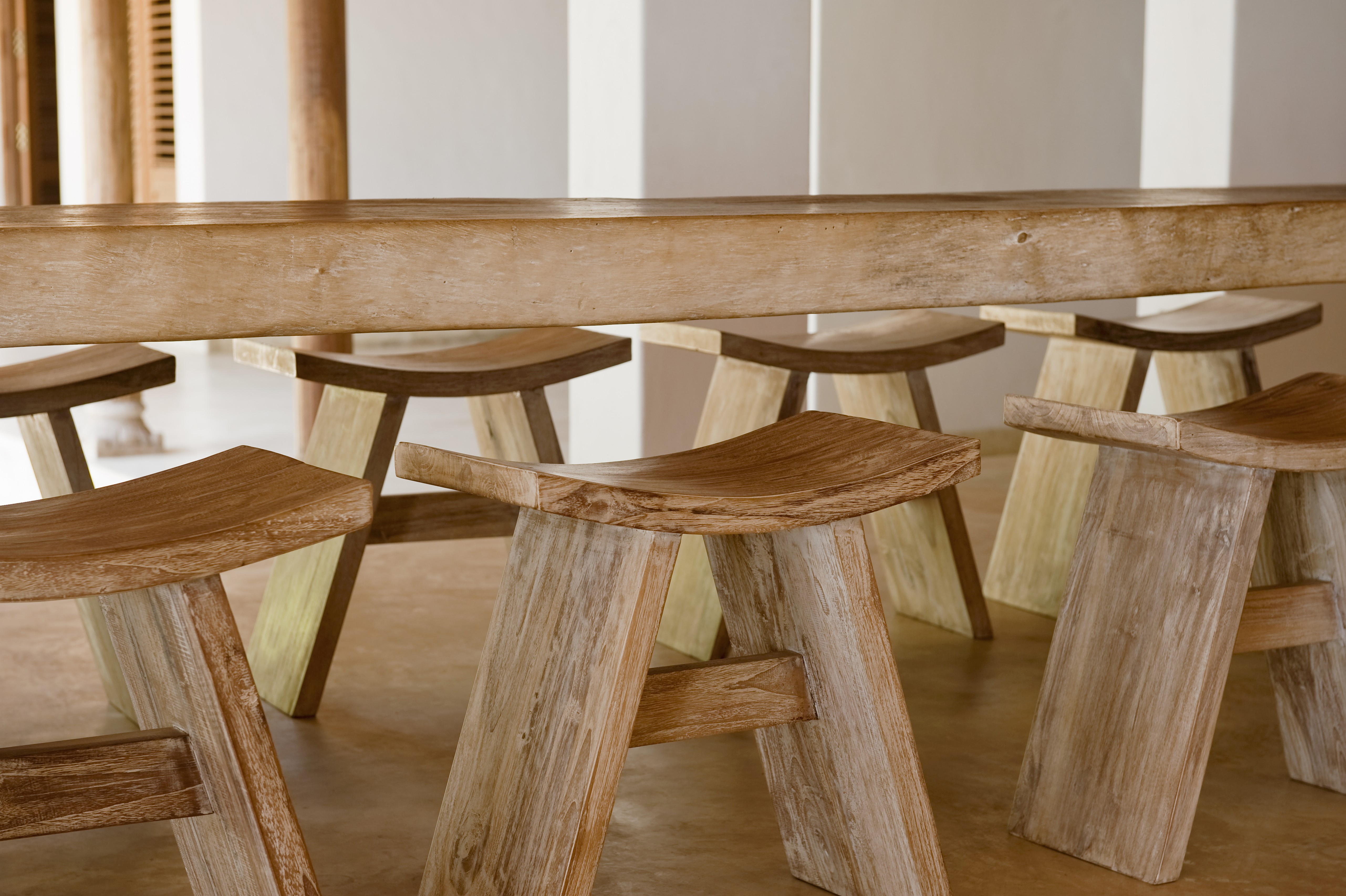 Mehrere hölzerne Hocker unter einem langen Holz-Esstisch.