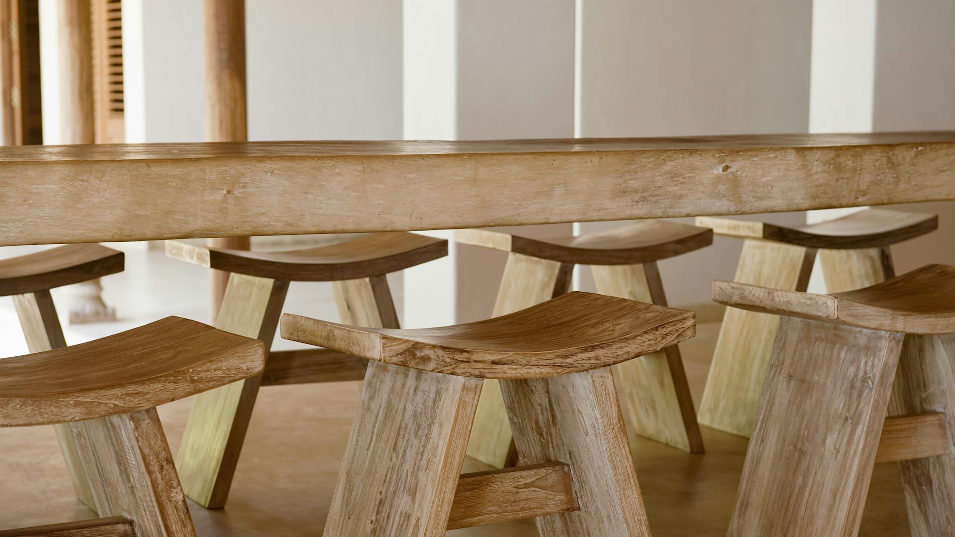 Mehrere hölzerne Hocker unter einem langen Holz-Esstisch.