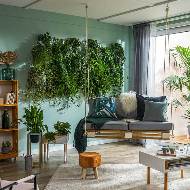 Palettenschaukel Baumelig hängt neben dem Kistenregal in einem Wohnzimmer mit einer bepflanzten Wand.