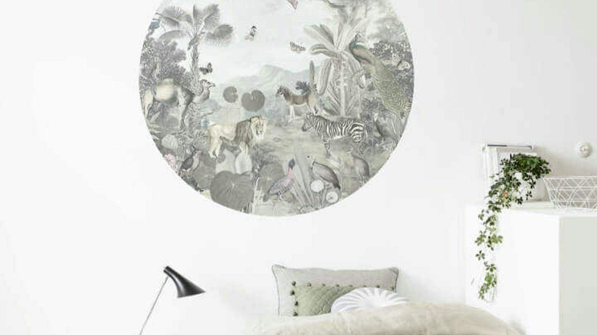 An der Wand, die sich hinter einem Bett und einem tiefen Ablagetisch befindet, klebt eine runde Tapete mit Dschungelmotiv mit Tieren an der Wand.