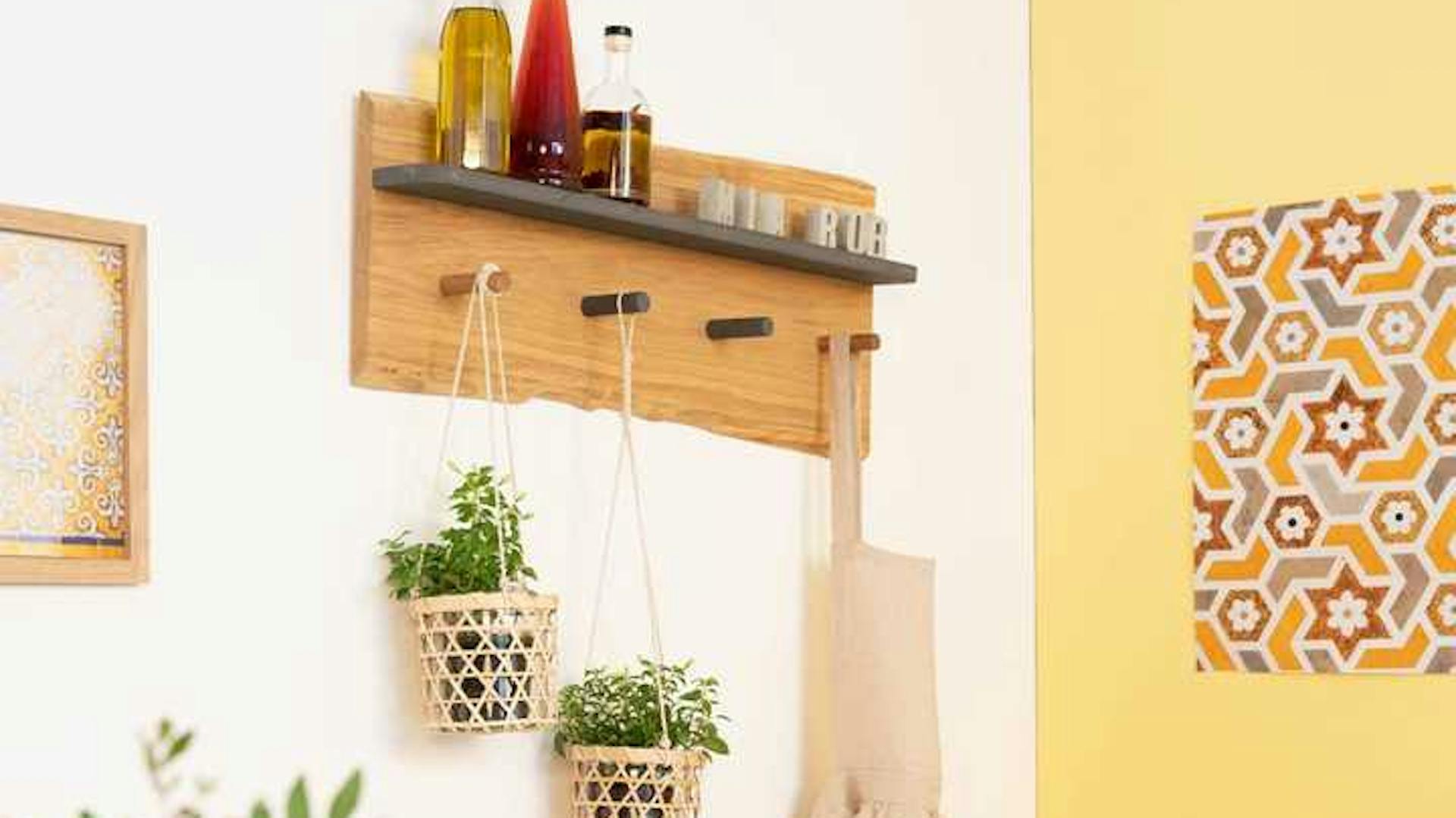 An einer weißen Wand hängt Garderobe Gerda, an ihr hängen Pflanzen sowie eine Schürze. Obendrauf stehen Flaschen.