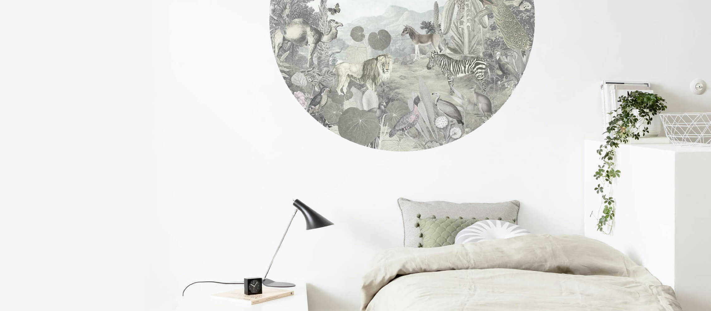 An der Wand, die sich hinter einem Bett und einem tiefen Ablagetisch befindet, klebt eine runde Tapete mit Dschungelmotiv mit Tieren an der Wand.