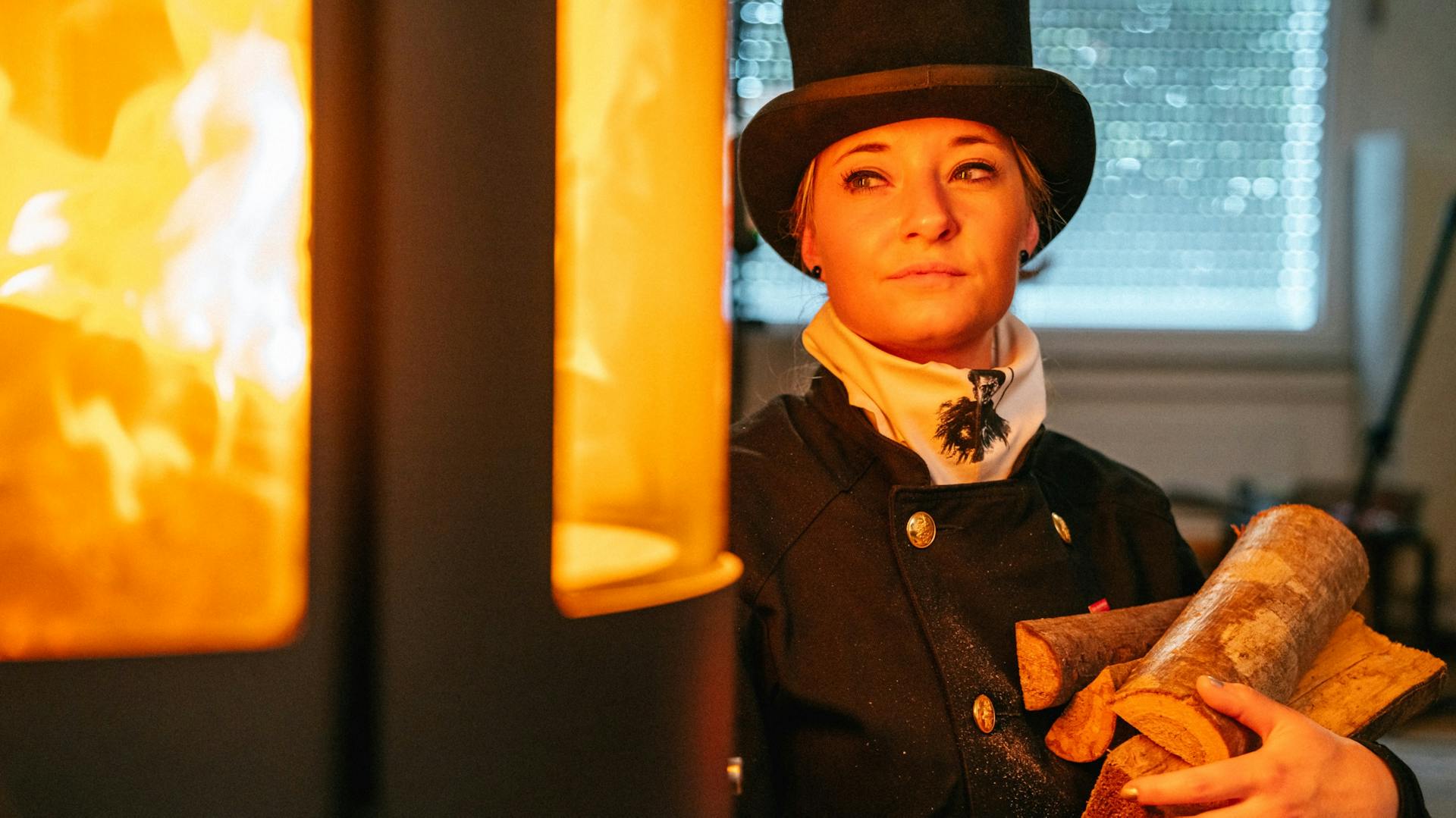 Eine Schornsteinfegerin beobachtet das brennende Feuer im Kamin.