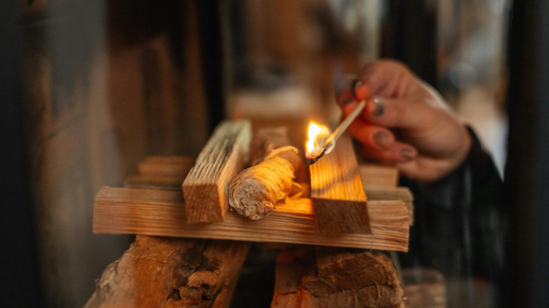 Mano con un fiammifero acceso su una catasta di legna