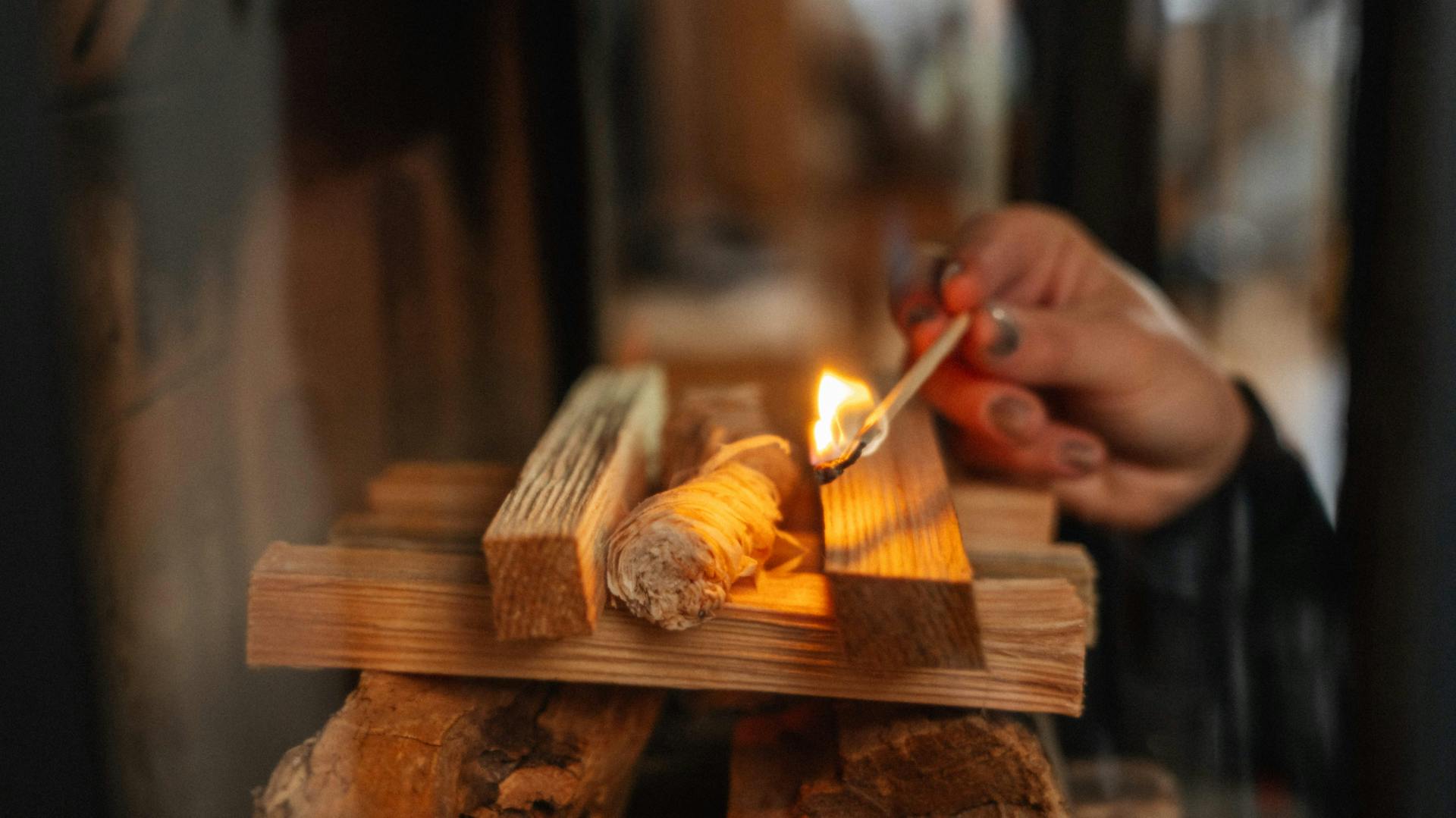 Im Brennraum des Kamins aufgestapelte Holzscheite werden mit einem Streichholz angezündet.