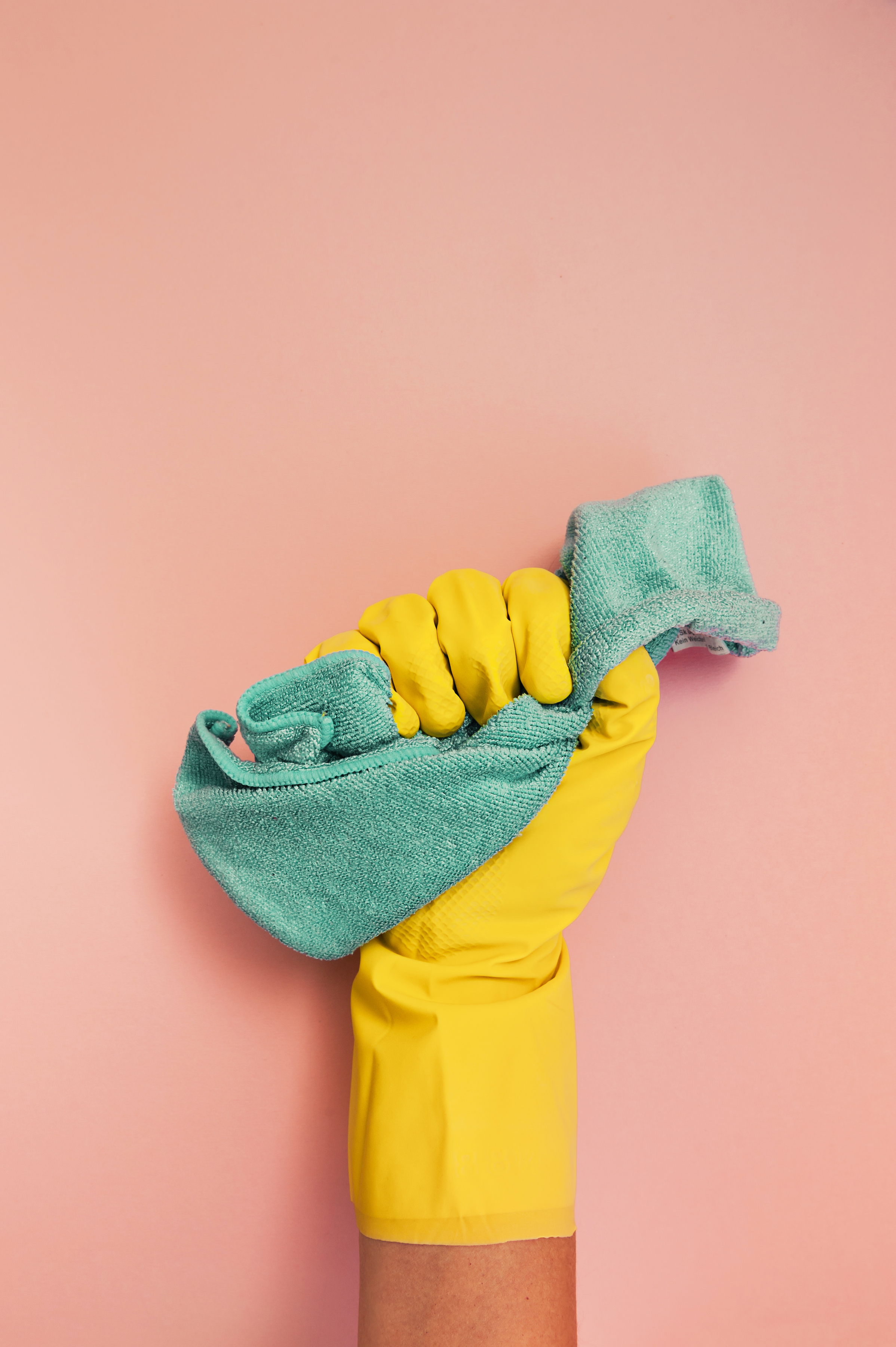 Mano con guanto giallo per le pulizie tiene un panno blu