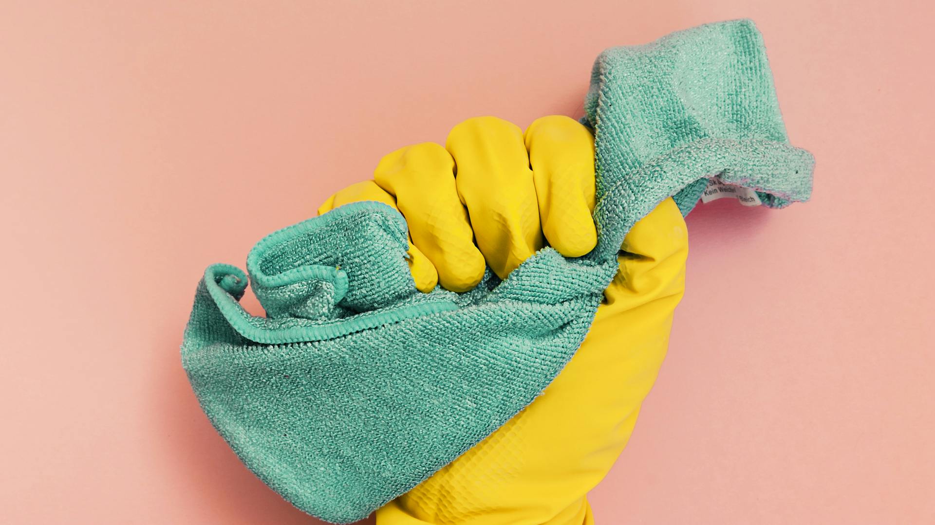 Mano con guanto giallo per le pulizie tiene un panno blu