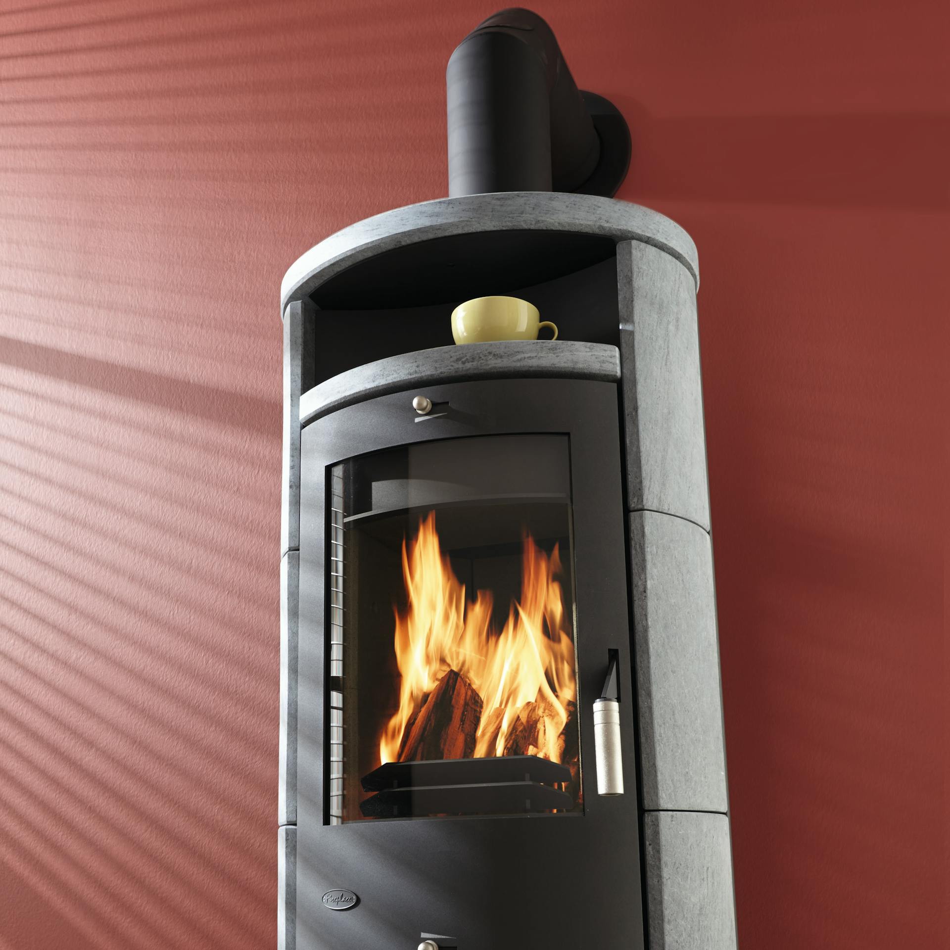 Stufa caminetto in pietra ollare con fuoco acceso davanti a una parete rossa