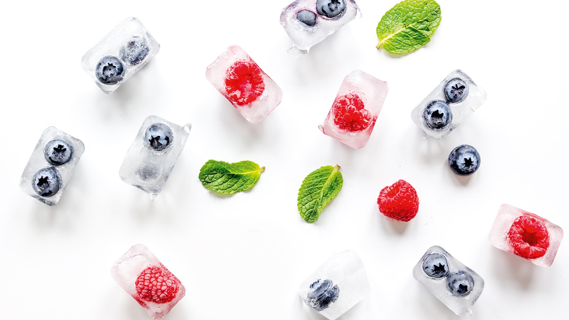 Színes jégkockák gyümölcsökkel, fehér háttéren.