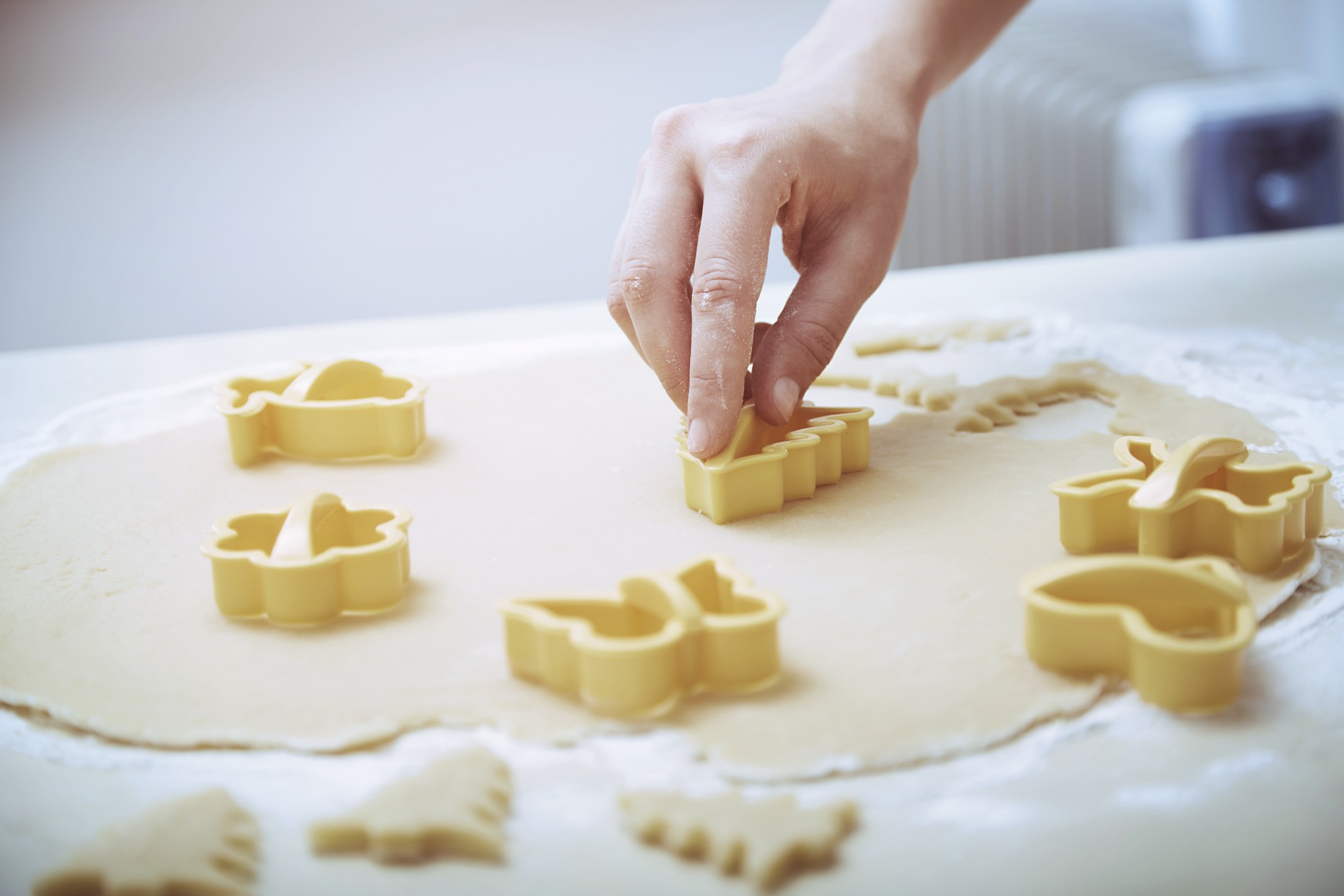 Kéz kekszeket szúr ki a tésztából kekszvágóval.