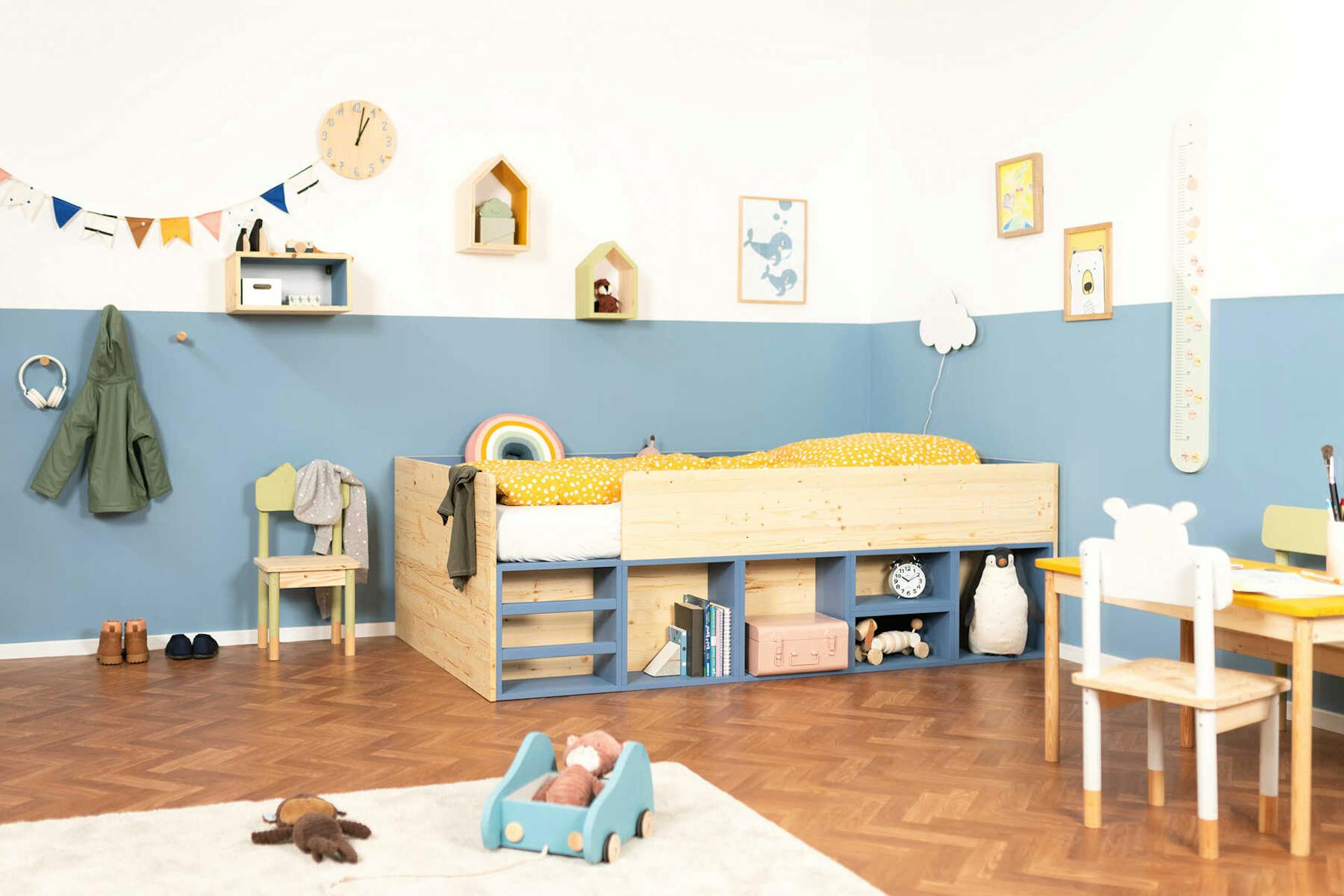 Frontansicht des aus Vollholz selbstgebauten Kinderbett Max in naturfarbe und blauen Regalböden mit Rausfallschutz.