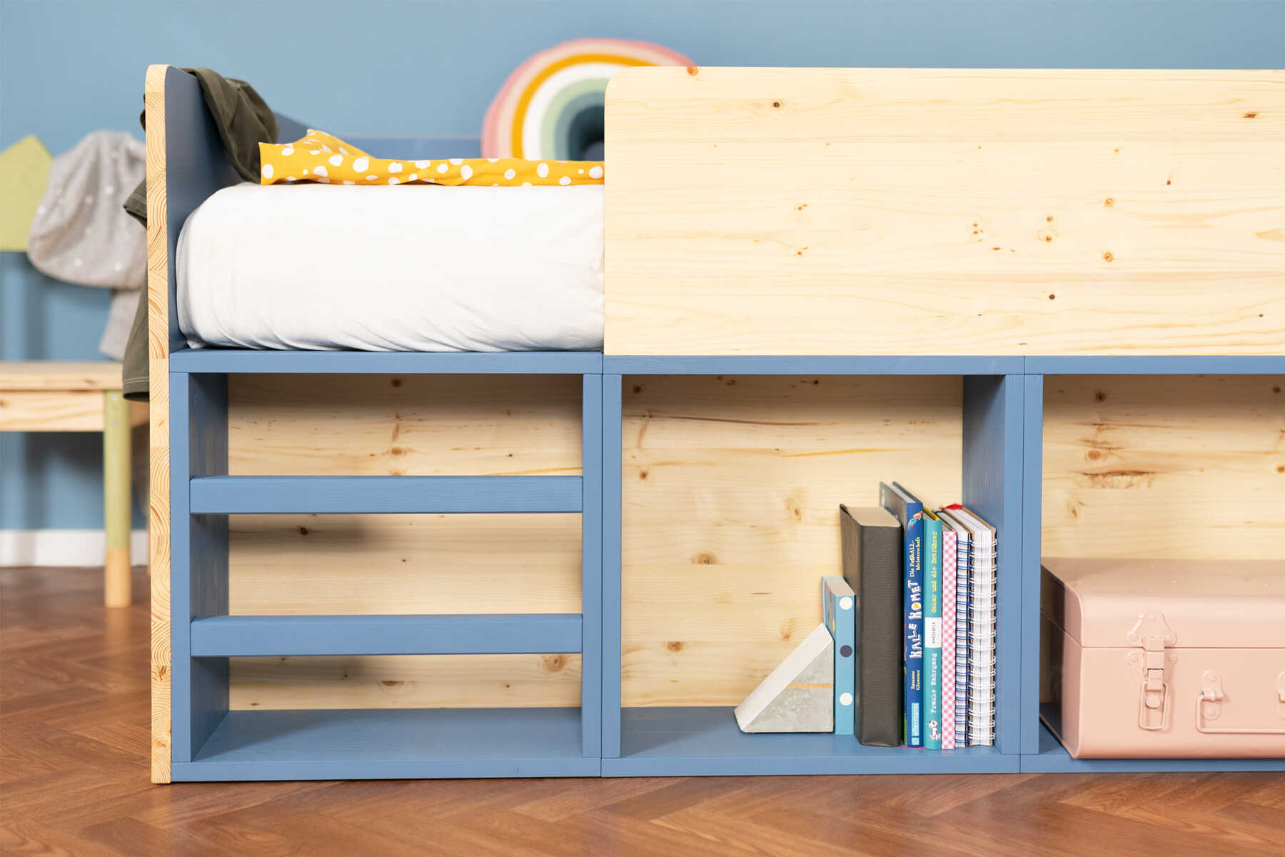 Detailansicht des aus Vollholz selbstgebauten Kinderbett Max in naturfarbe und blauen Regalböden mit Rausfallschutz.