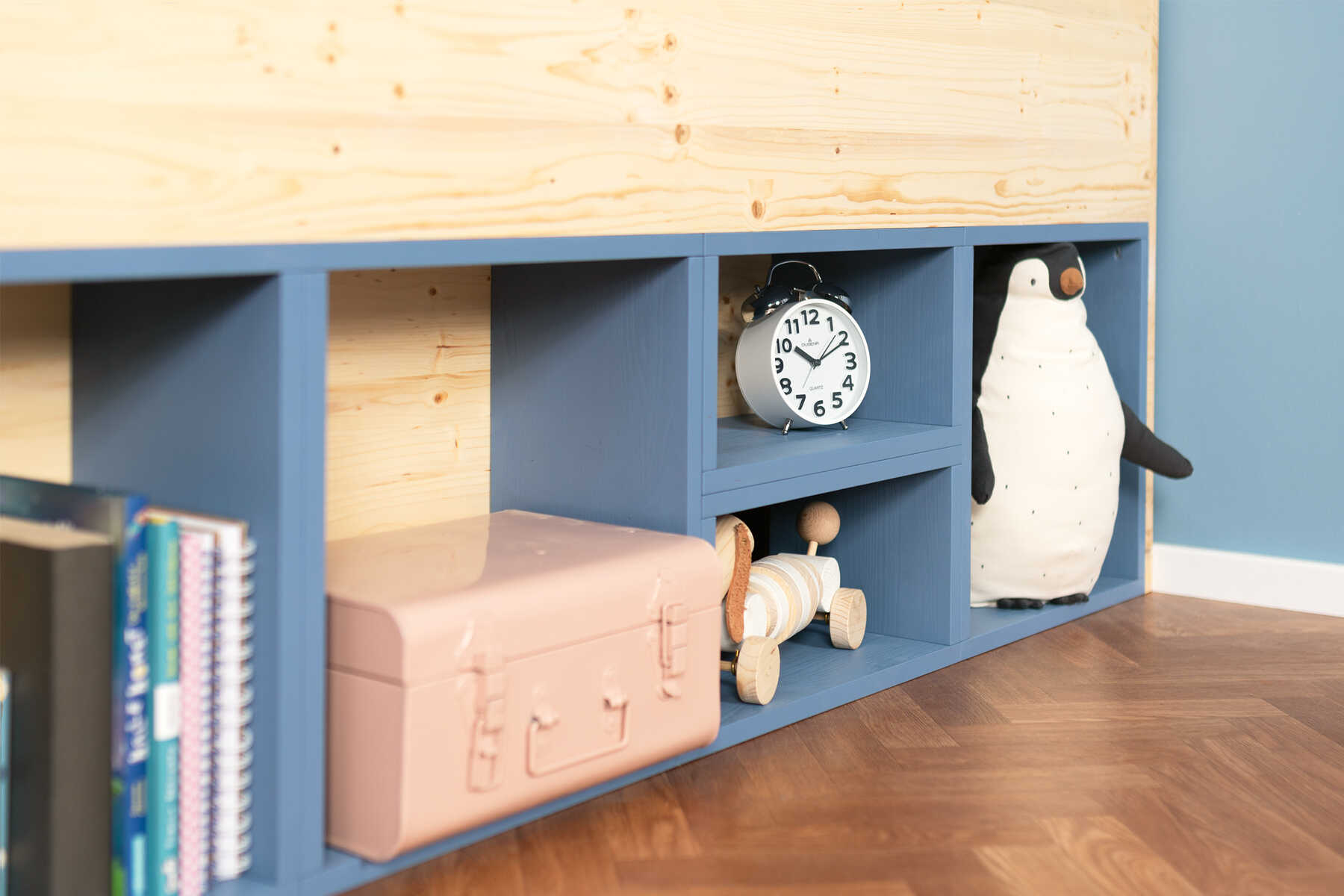 : Seitliche Detailansicht des aus Vollholz selbstgebauten Kinderbett Max in naturfarbe und blauen Regalböden mit Rausfallschutz.