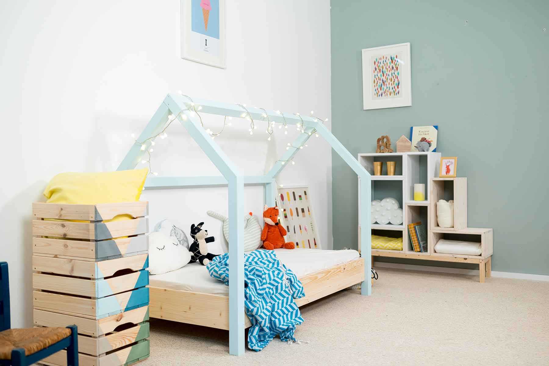 Seitliche Ansicht des spielhausförmigen Kinderbetts Moritz mit hellblauen Balken.