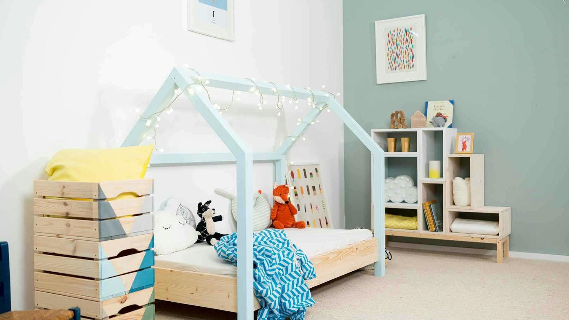 Seitliche Ansicht des spielhausförmigen Kinderbetts Moritz mit hellblauen Balken.