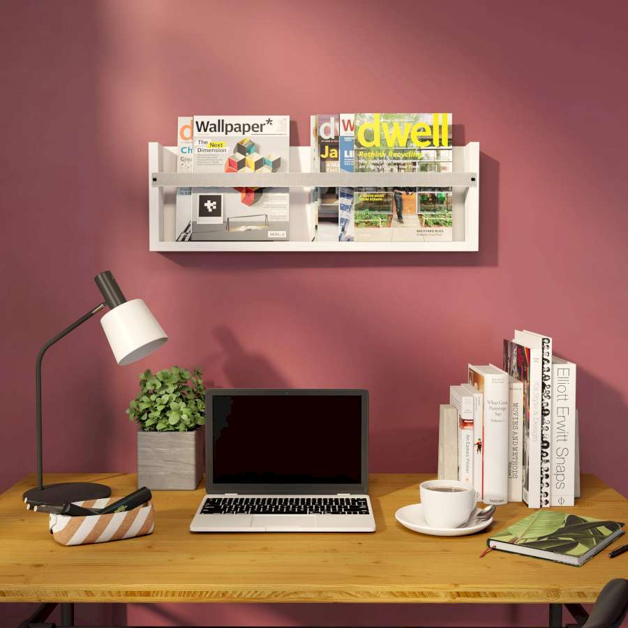 Es hängt ein Magazinregal an einer roten Wand über einem Schreibtisch.