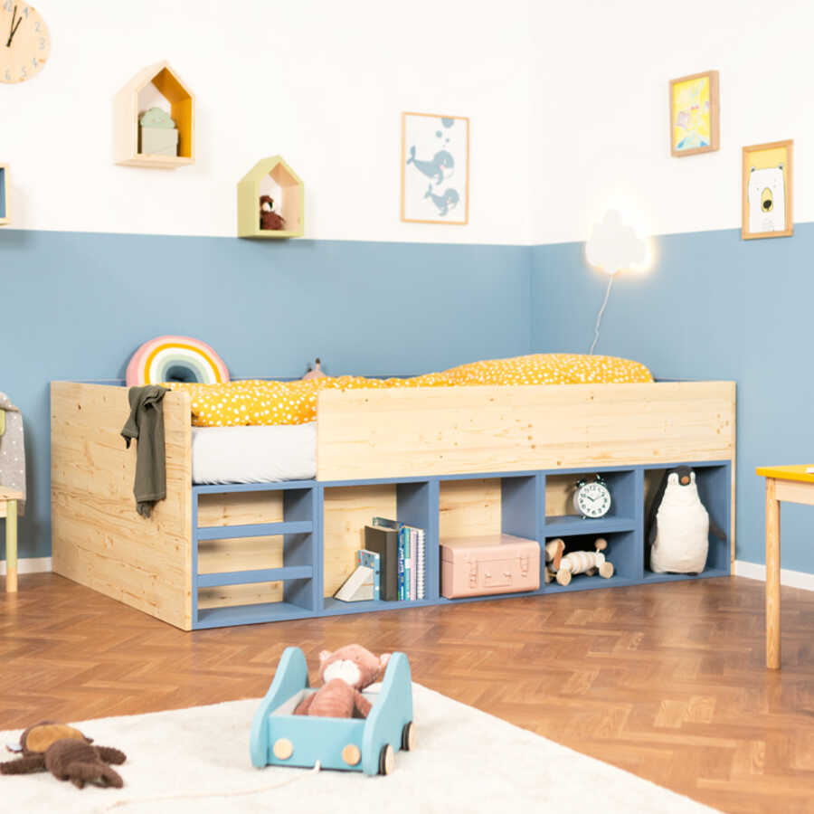 Das Holz-Kinderbett Mac steht vor einer zur Hälfte blau gestrichenen Wand in einem Kinderzimmer.