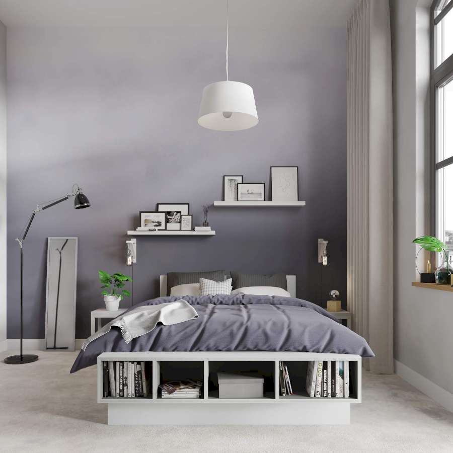 An einer grauen Ombré Wand hängen Regale, auf den Bilder platziert sind. Vor stehen ein weißes Bett mit grauem Bezug, Nachtische, ein Spiegel und eine Stehlampe.