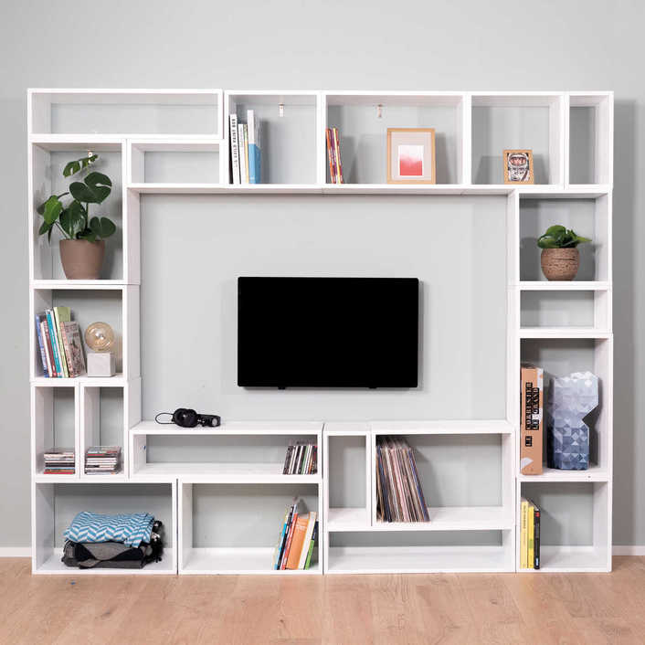 In der Mitte eines weißen Regals ist ein Fernseher. Das Regal ist gefüllt mit Büchern, Dekoration und Pflanzen.