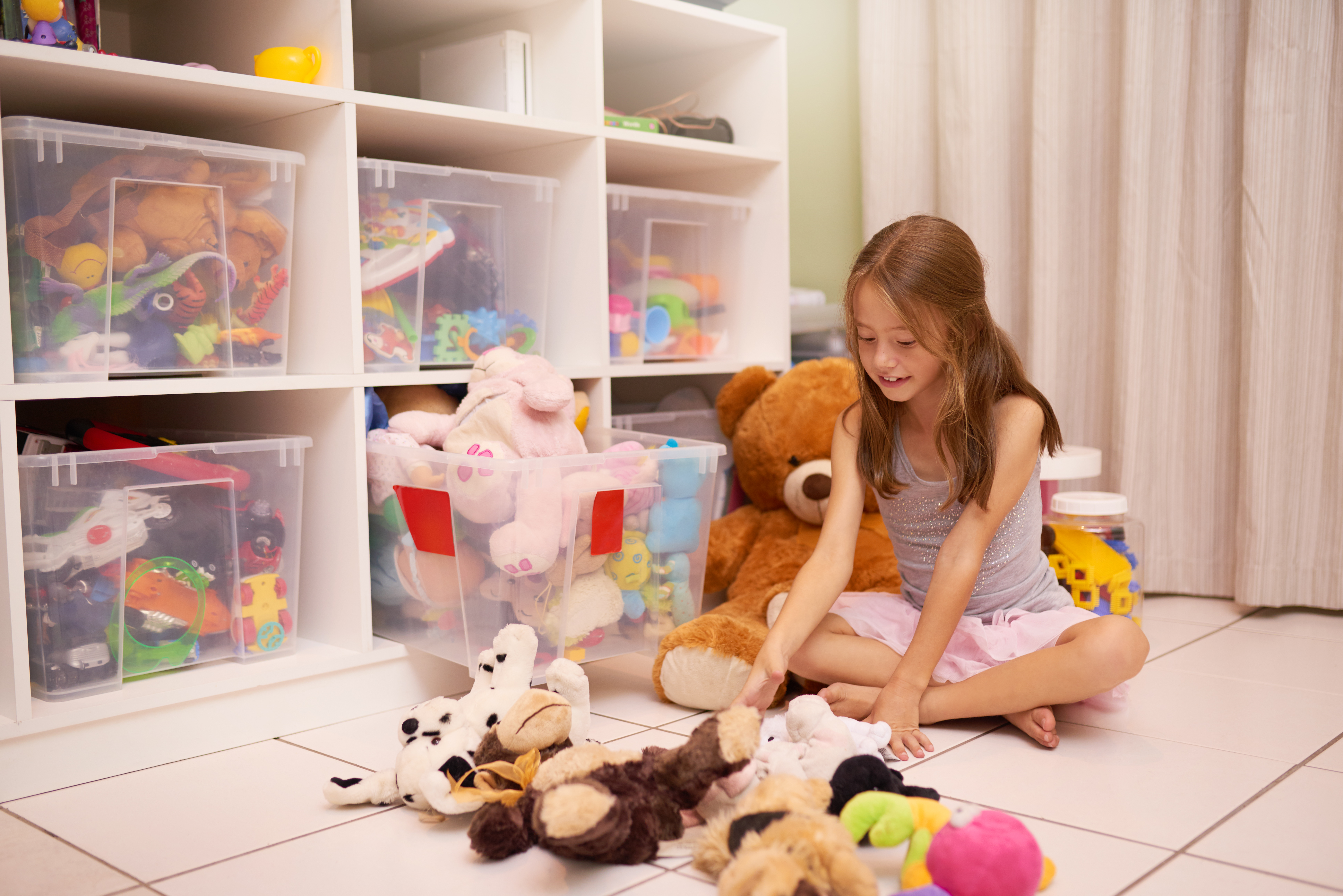 Kind spielt mit Stofftieren in Kinderzimmer neben Regal mit Aufbewahrungsboxen.