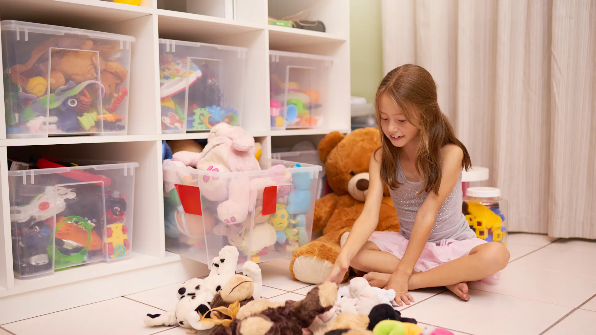 Kind spielt mit Stofftieren in Kinderzimmer neben Regal mit Aufbewahrungsboxen.