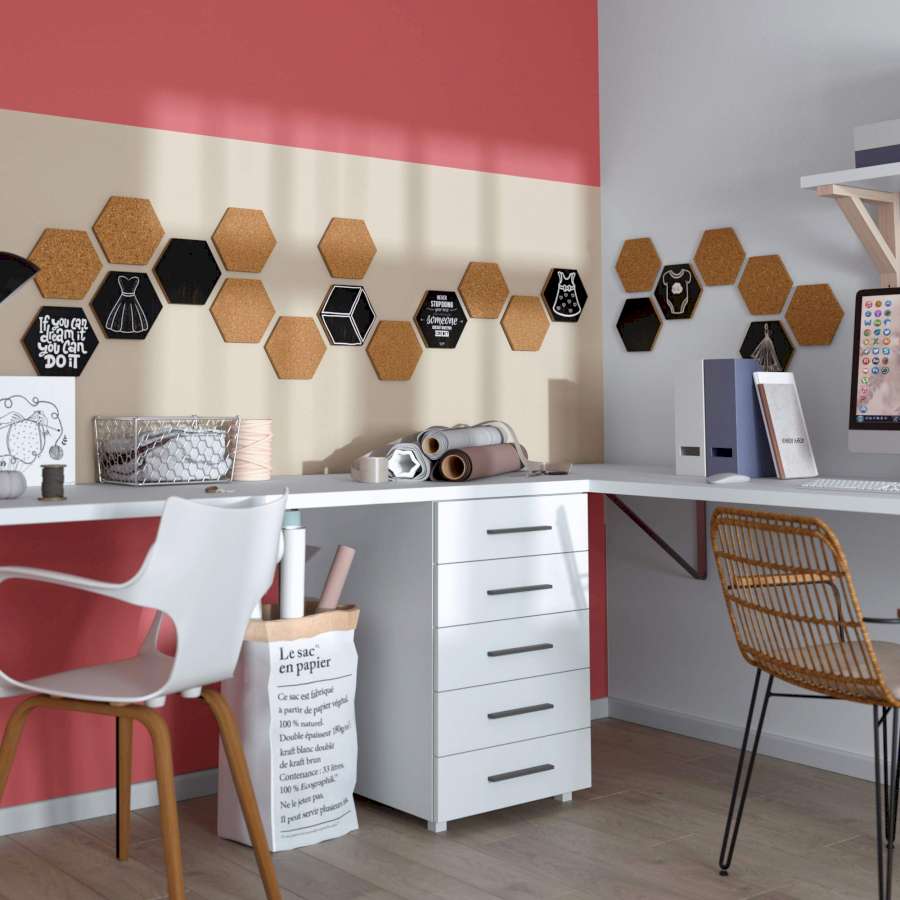 An einer Wand hängt eine Pinnwand aus vielen Korkhexagonen. Davor stehen zwei Schreibtische mit Arbeitsmaterialien zum Nähen und für Büroarbeit.