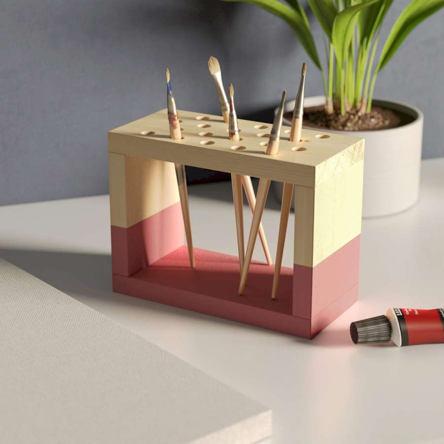 Auf einem Tisch steht ein Pinselhalter, der zur Hälfte rosa bemalt ist.