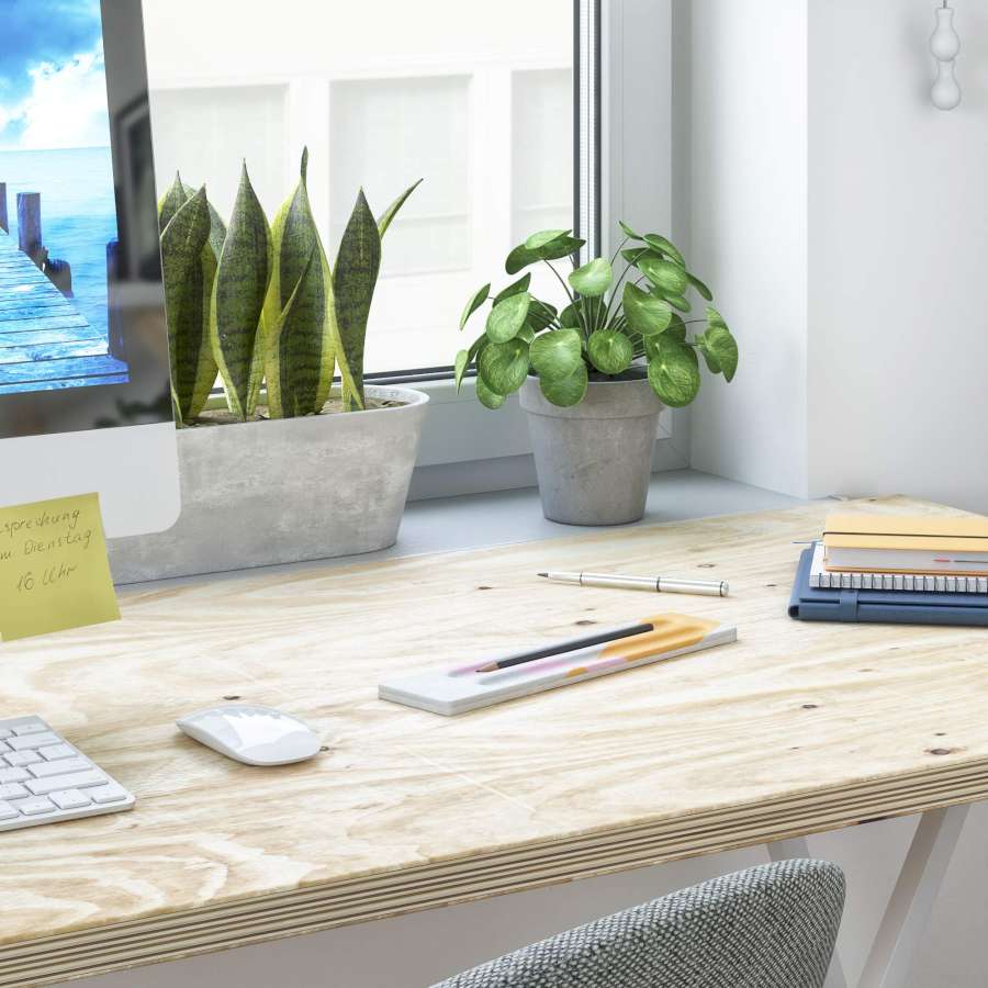 Auf einem Schreibtisch liegt zwischen Büromaterialien eine bunte Stiftablage aus Knetbeton. Im Hintergrund sind Pflanzen und ein Fenster.