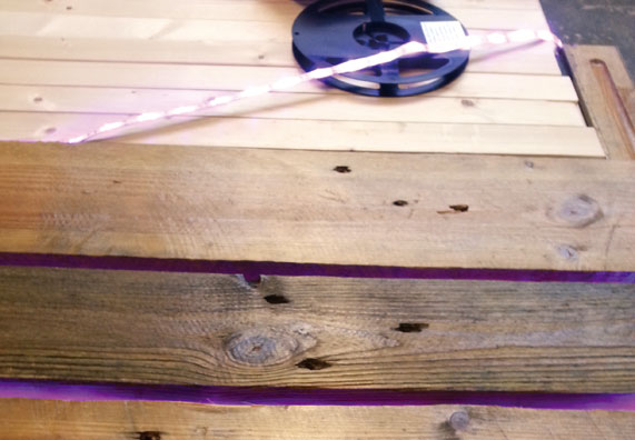 Leuchtender LED-Streifen hinter den Latten verklebt, daneben liegt die Rolle mit dem LED-Band.