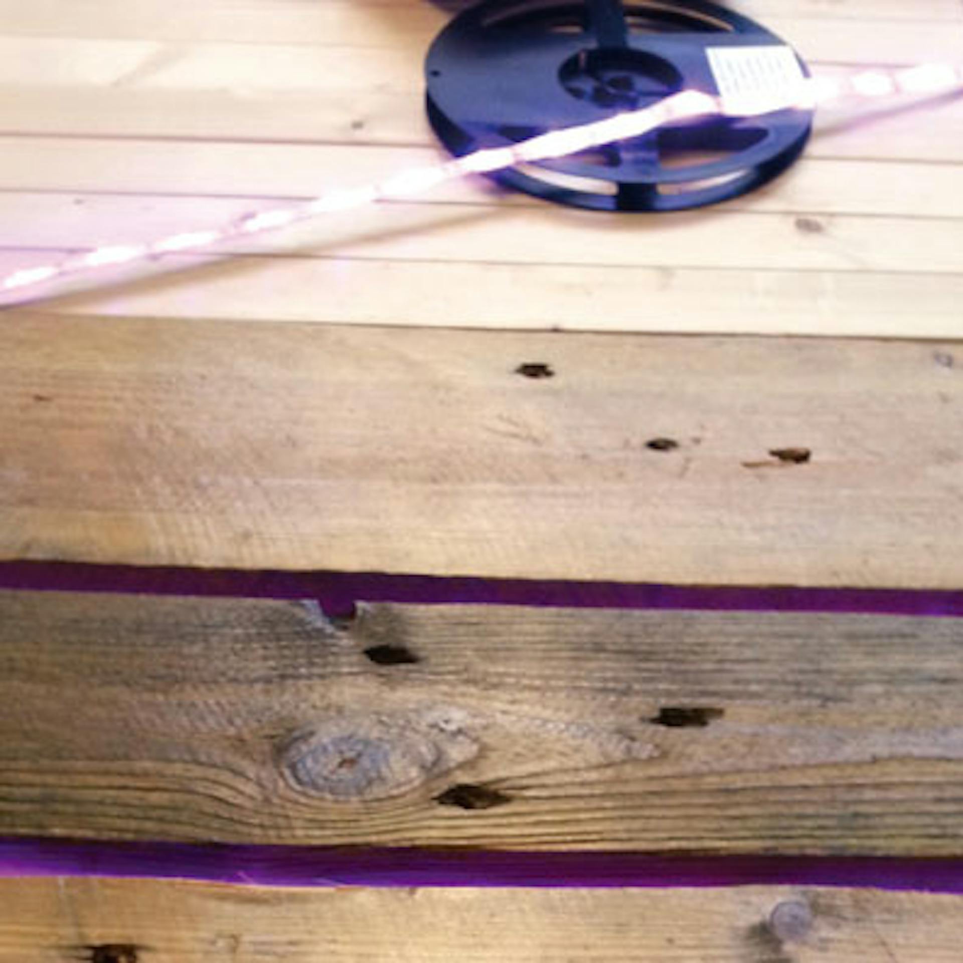 Leuchtender LED-Streifen hinter den Latten verklebt, daneben liegt die Rolle mit dem LED-Band.