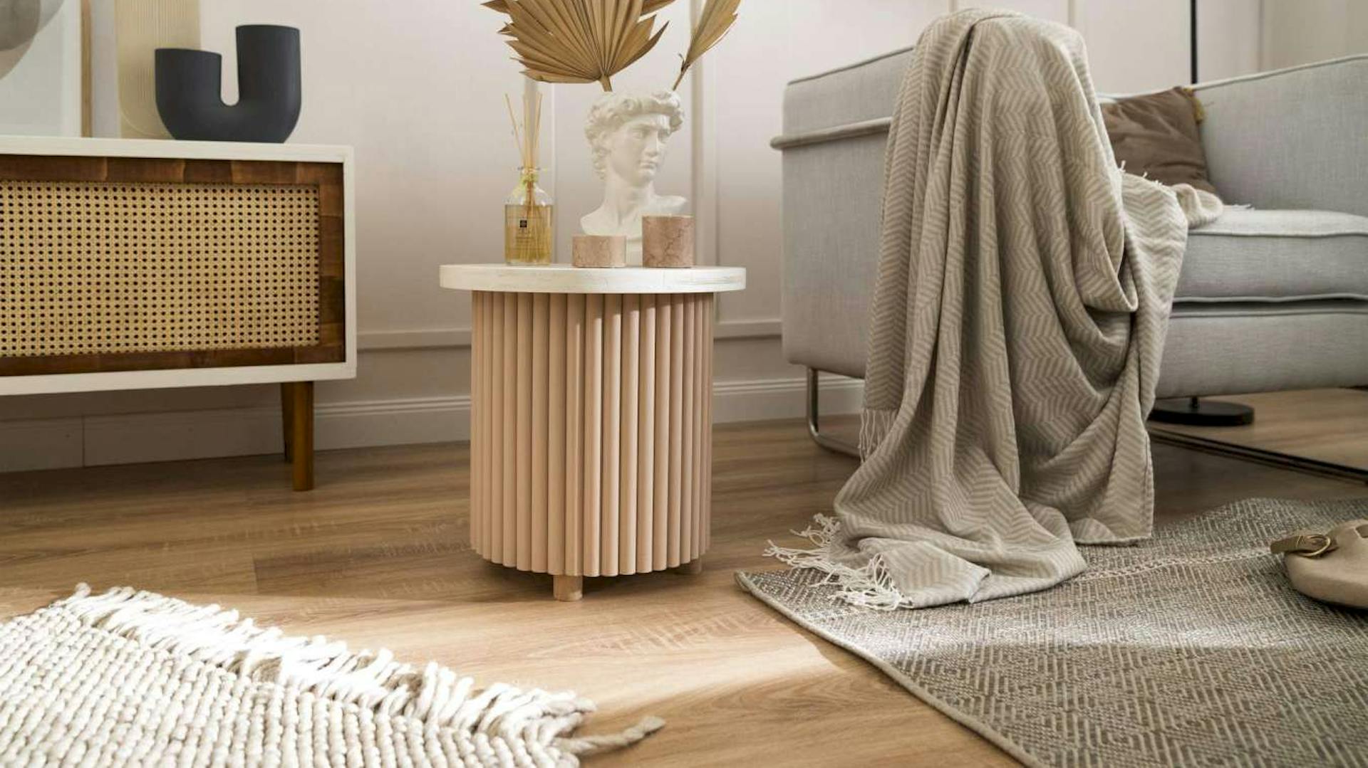 Ein Beistelltisch mit Lamellen zwischen einem Regal und einer Couch in einem Wohnzimmer