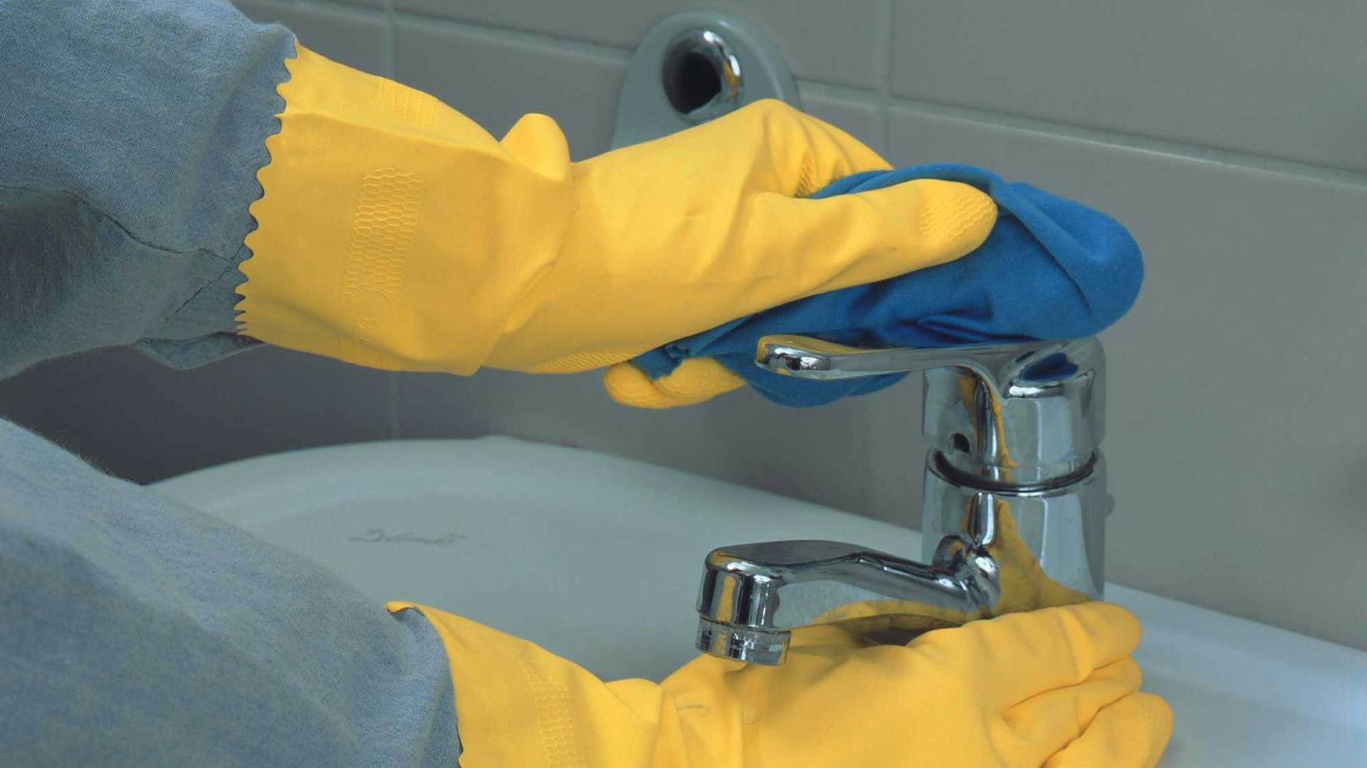 Jemand reinigt mit Handschuhe und Tuch einen Wasserhahn