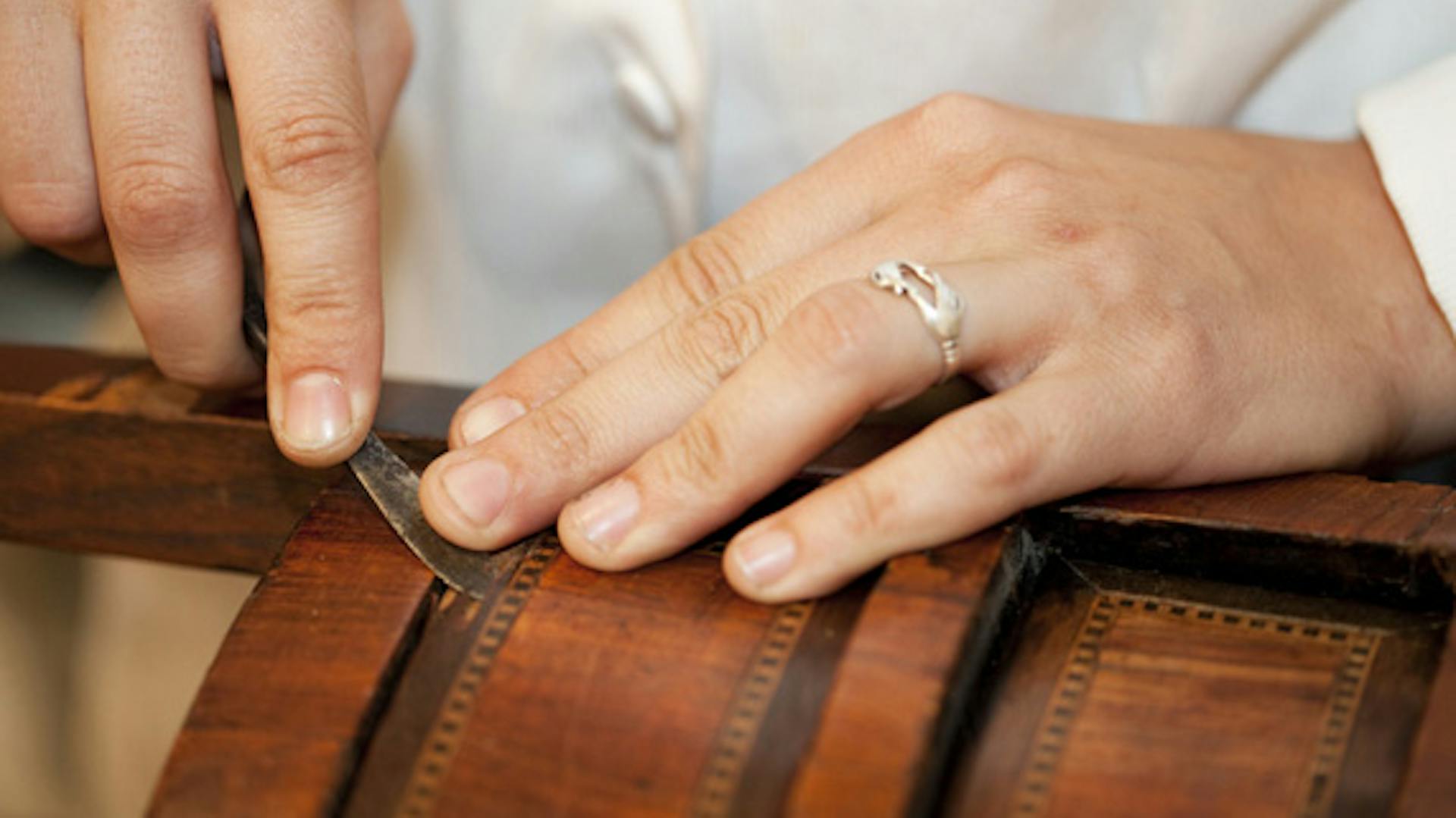 Egy ember régi furnért javít egy antik bútoron.