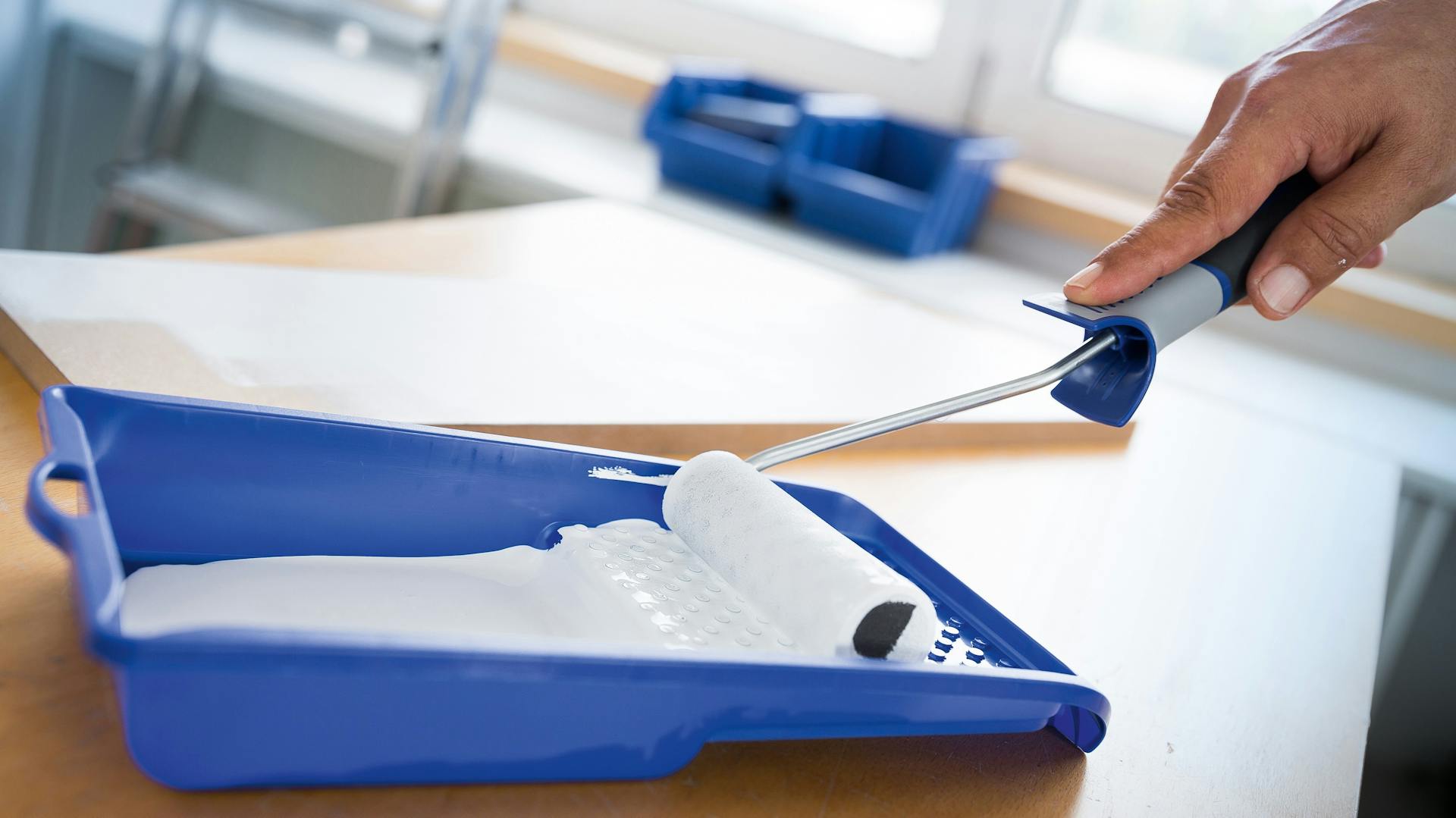 Jemand rollt einen Farbroller in einer Farbwanne.