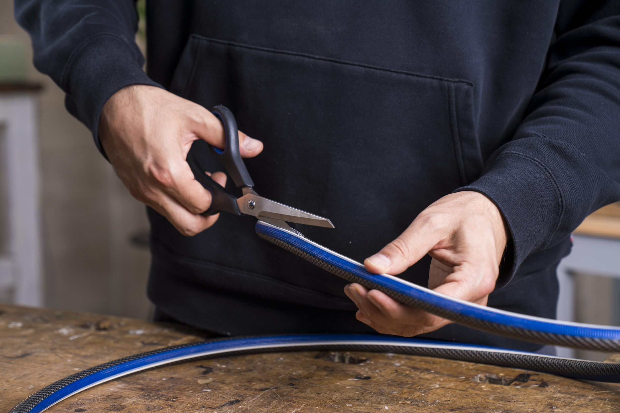 Tmavá záhradná hadica sa v strede prestrihne nožnicami.