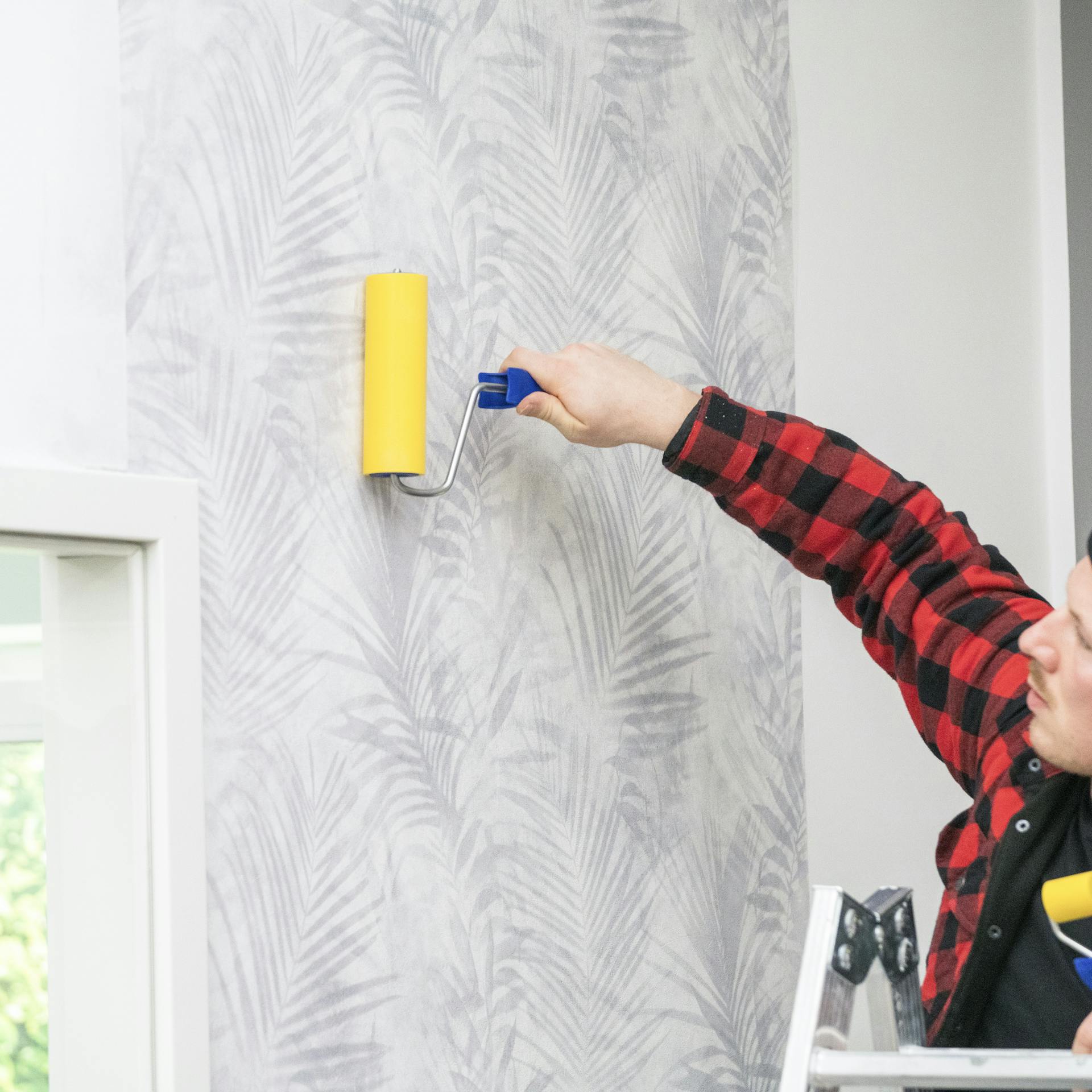 Ein Mann drückt Tapete an der Wand mit einem Moosgummi-Roller an.