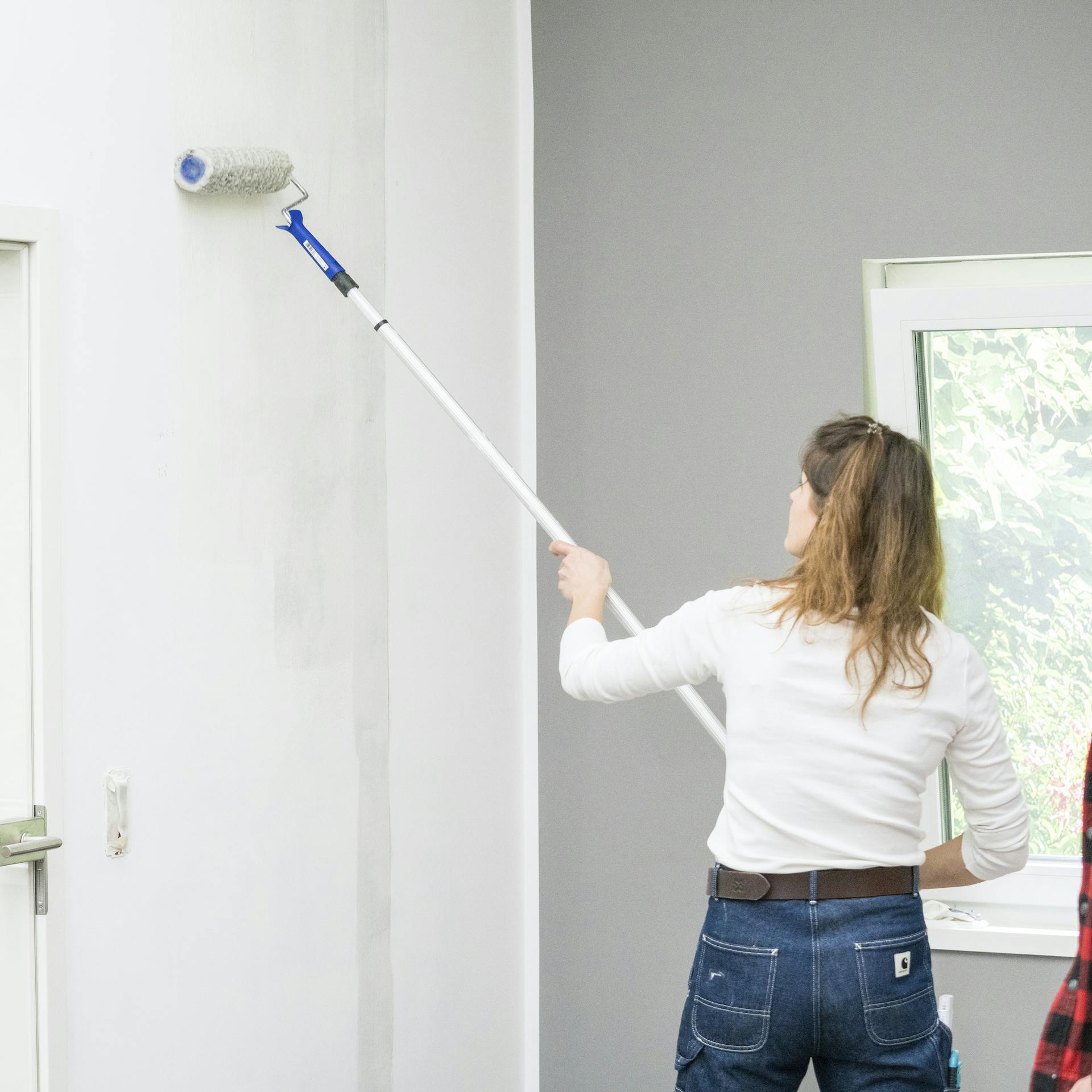 Eine Frau trägt Tapetengrund mit einer Malerrolle auf.