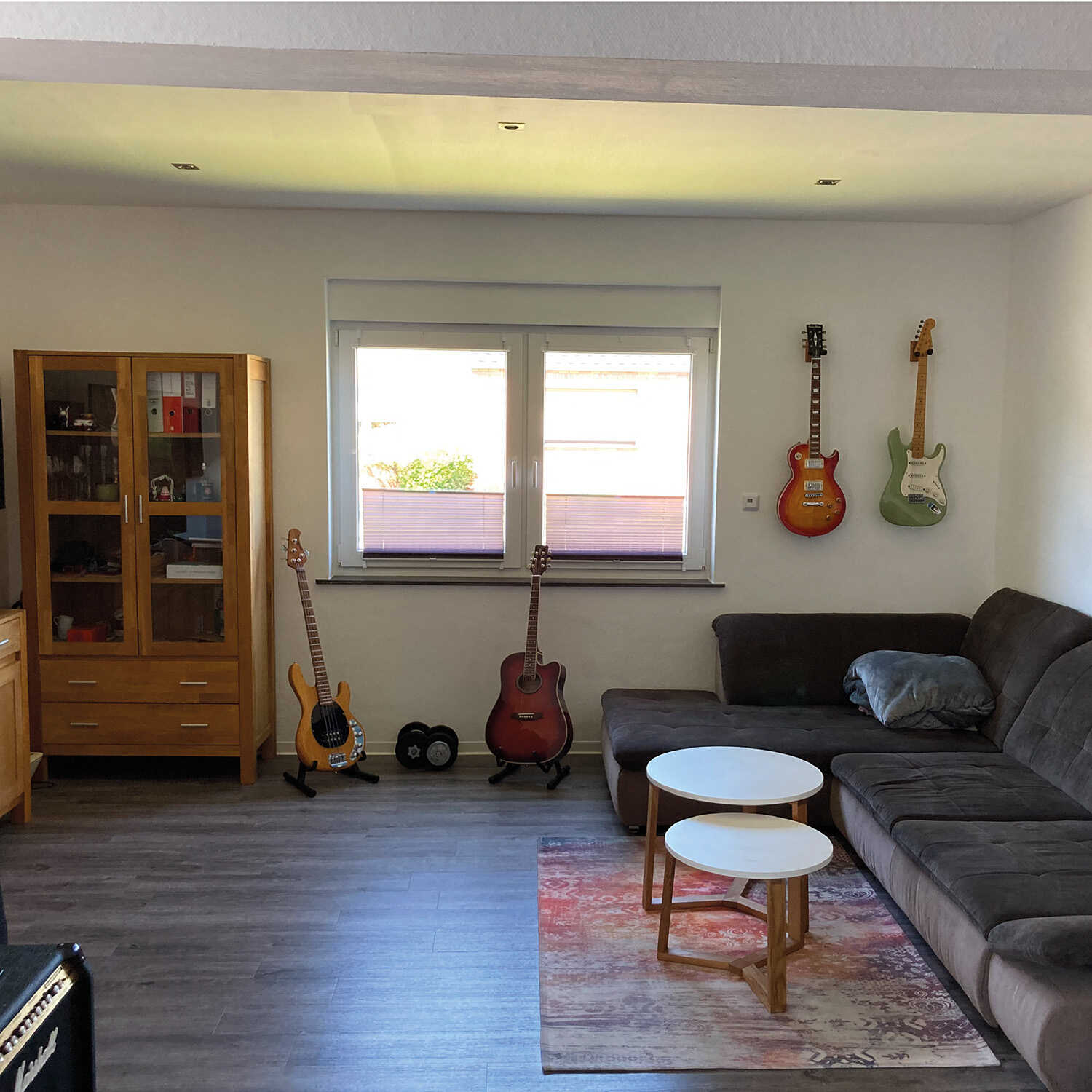 In einem dunkel wirkenden Musikzimmer steht eine Couch, darüber und daneben befinden sich Gitarren. Vor der Couch steht ein Beistelltisch.