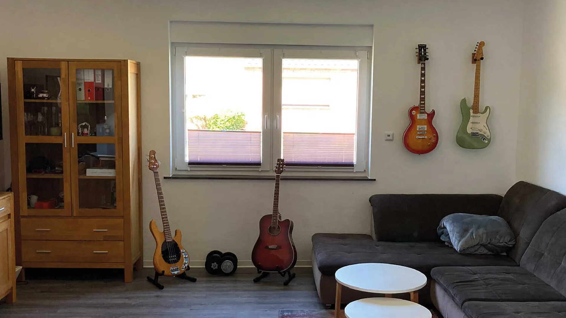 In einem dunkel wirkenden Musikzimmer steht eine Couch, darüber und daneben befinden sich Gitarren. Vor der Couch steht ein Beistelltisch.