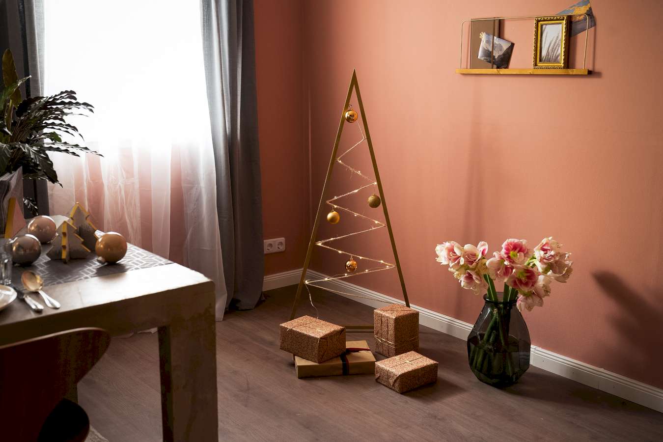 Vor einer orangenen Wand steht ein moderner Weihnachtsbaum aus Holzleisten. Davor liegen einige Geschenke.