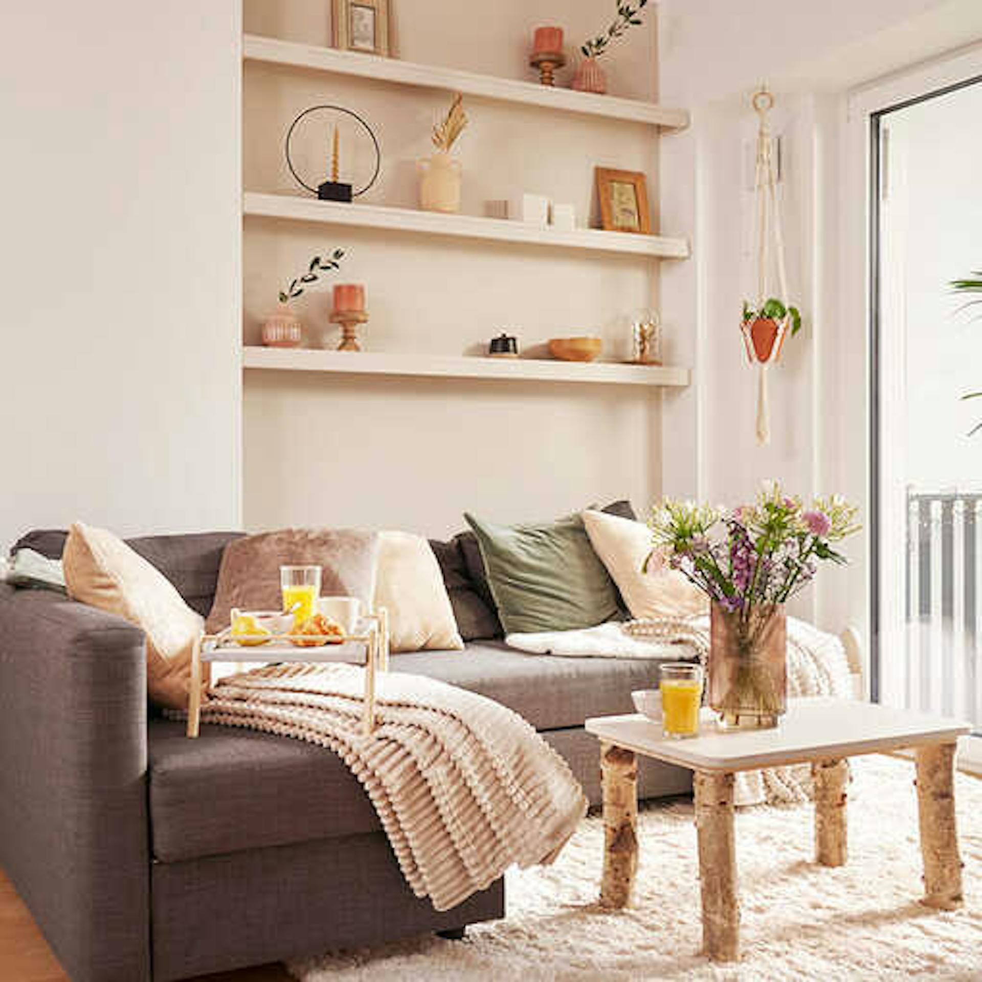 Ein Wohnzimmer in hellen Farben. Vor der grauen Couch steht ein Couchtisch aus Holz.