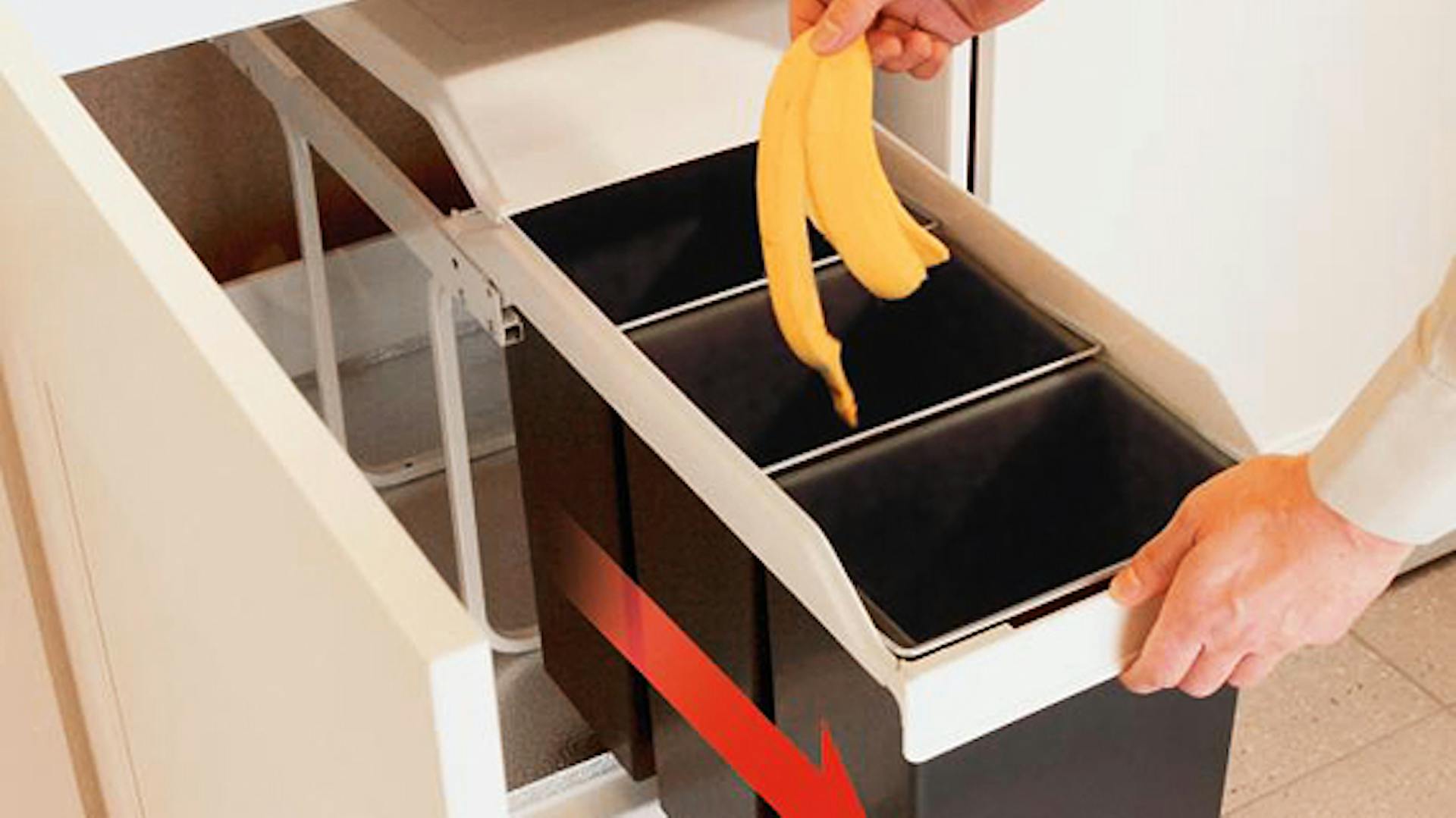 Jemand wirft eine Bananenschaler in einen ausziehbaren Mülleimer mit drei Fächern.