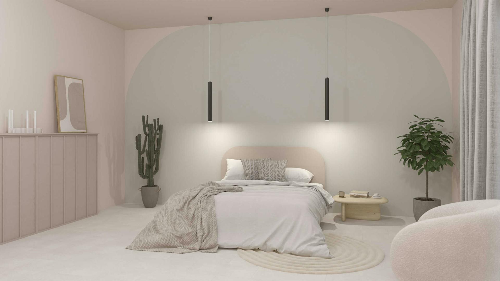 Ein Schlafzimmer, das in Weiß und Beige gestaltet wurde. Es steht zentral ein Bett vor der Wand, die mit einer großen Farbfläche gestaltet wurde. Daneben befinden sich ein Nachttisch, ein Sessel, ein Regal und Pflanzen.