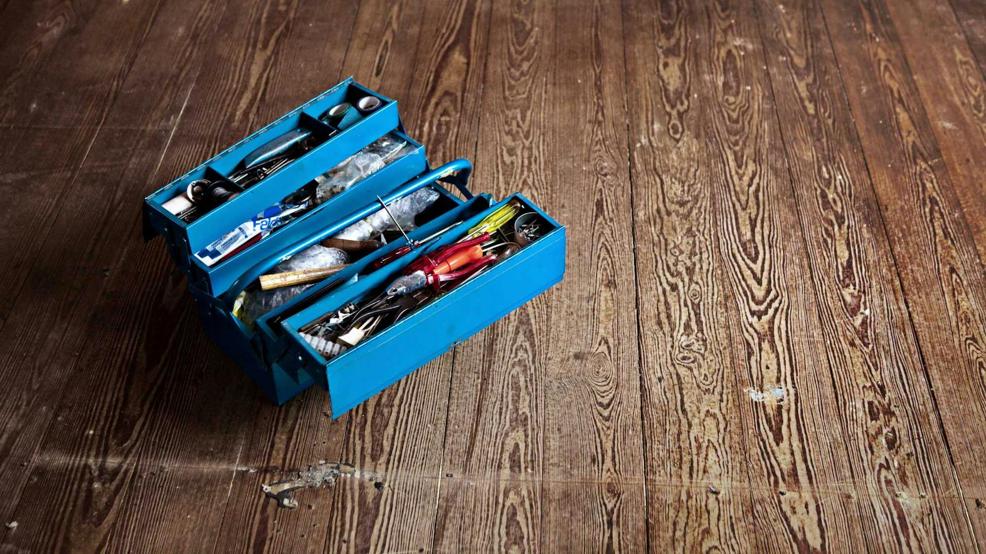 Gefüllter blauer Werkzeugkasten auf dunklem, beschädigten Parkett