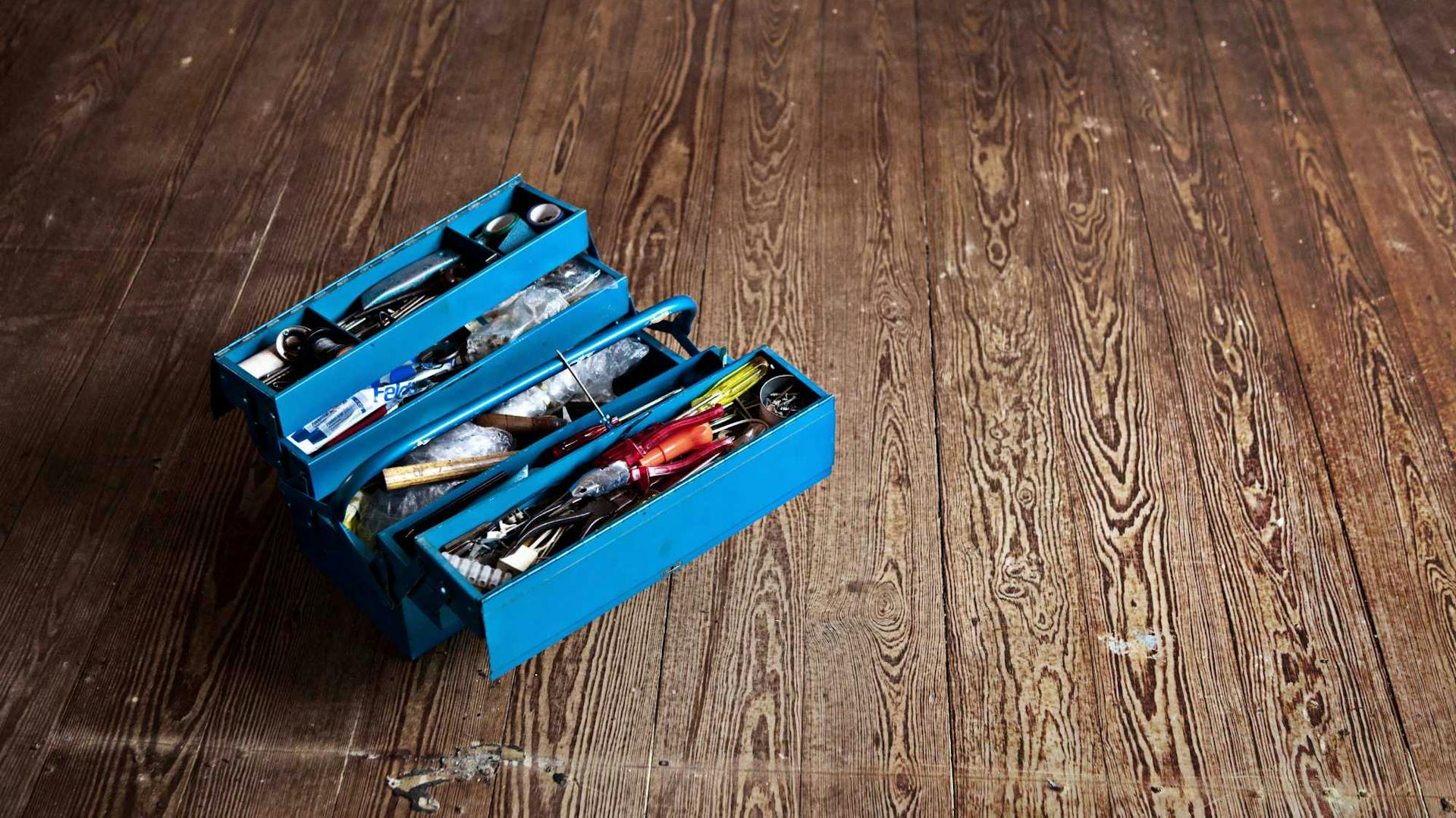 Gefüllter blauer Werkzeugkasten auf dunklem, beschädigten Parkett