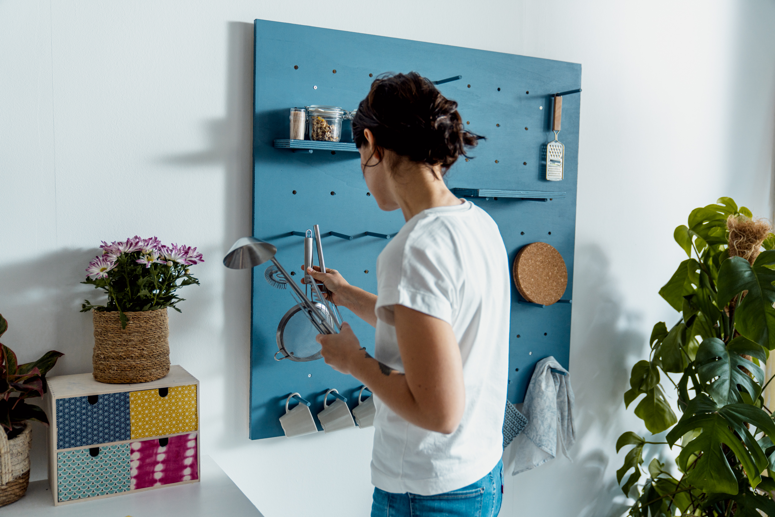 Person bestückt fertiges Pegboard mit Küchenutensilien.