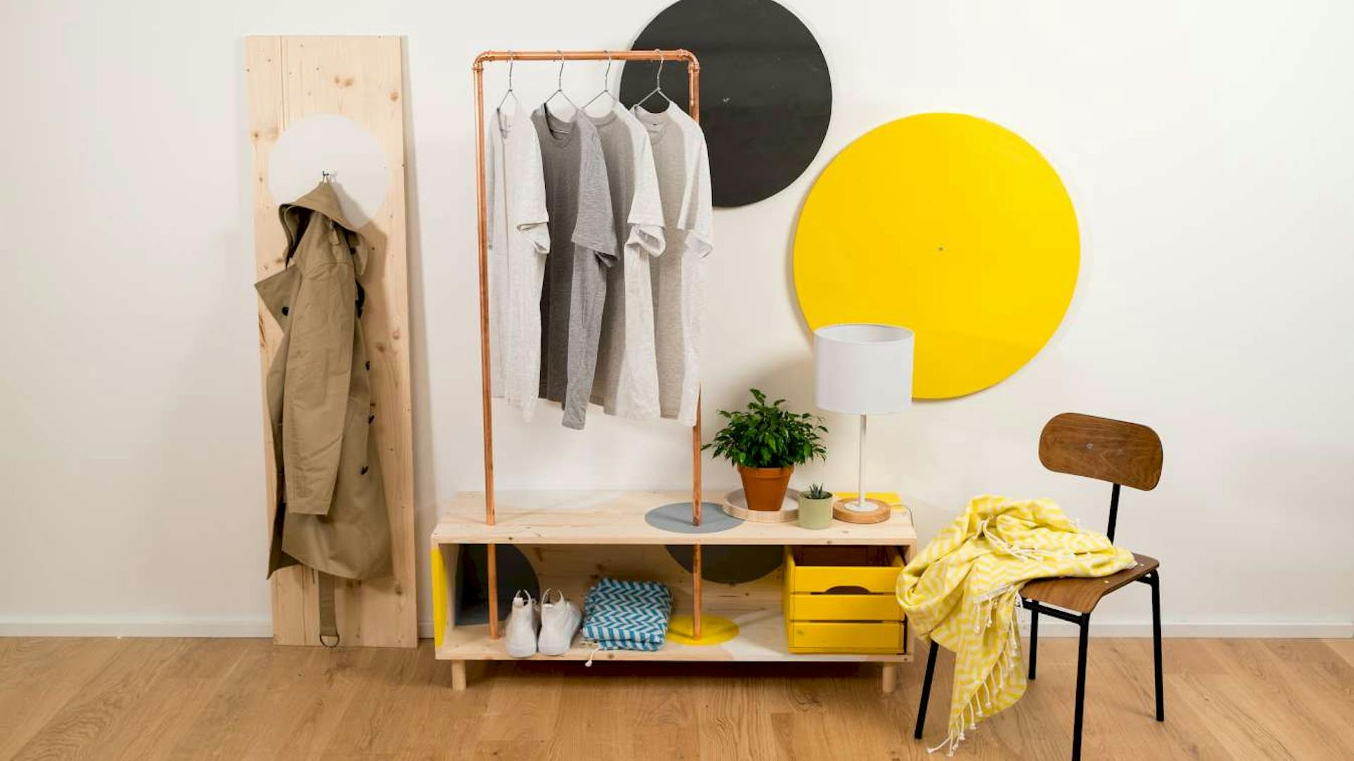 An einer weißen Wand sind graue und gelbe Kreise befestigt. Davor sind eine Garderobe und ein Stuhl platziert.