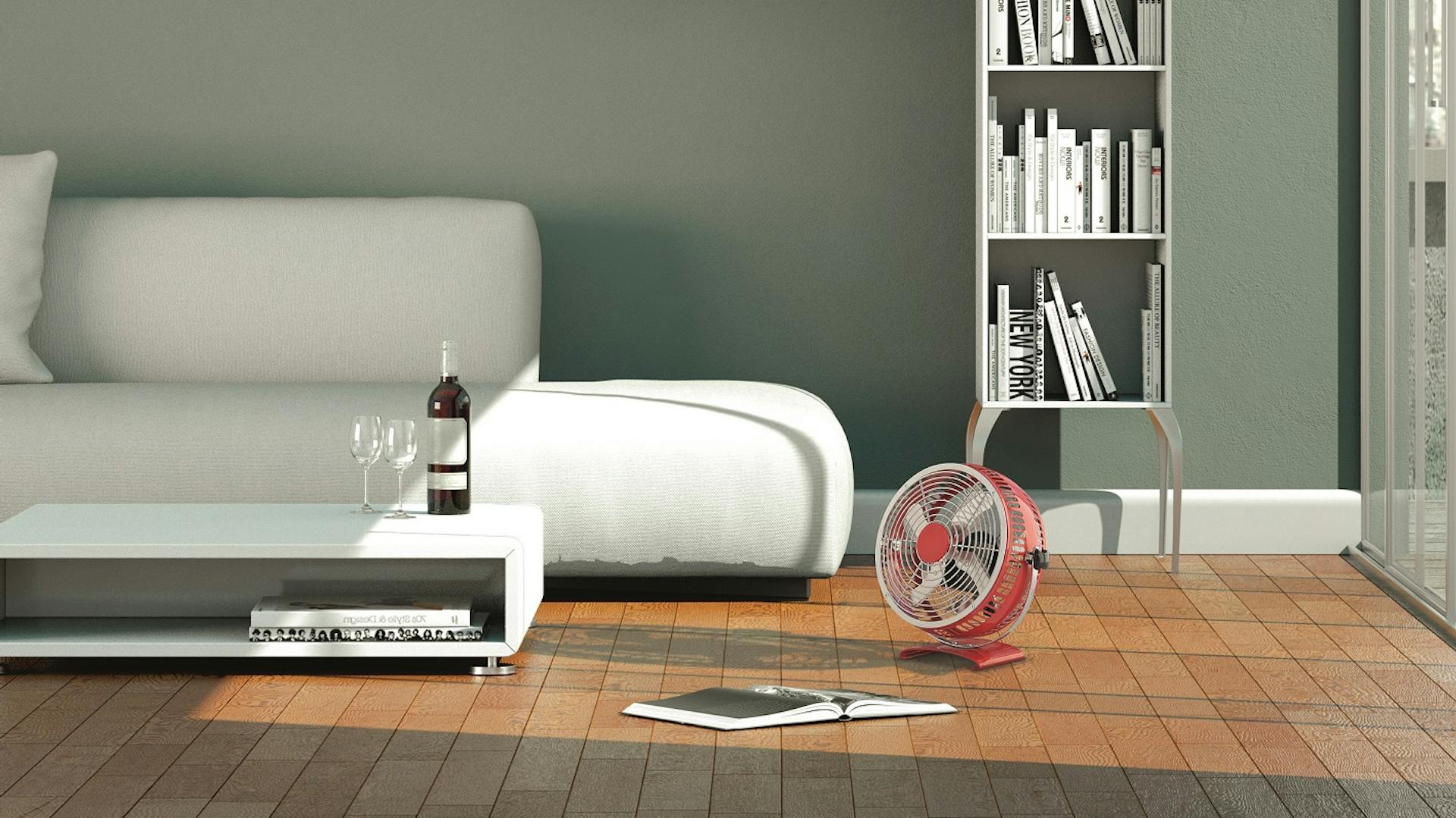 Ein roter Bodenventilator steht in einem Zimmer mit Bücherregal und weißem Sofa.