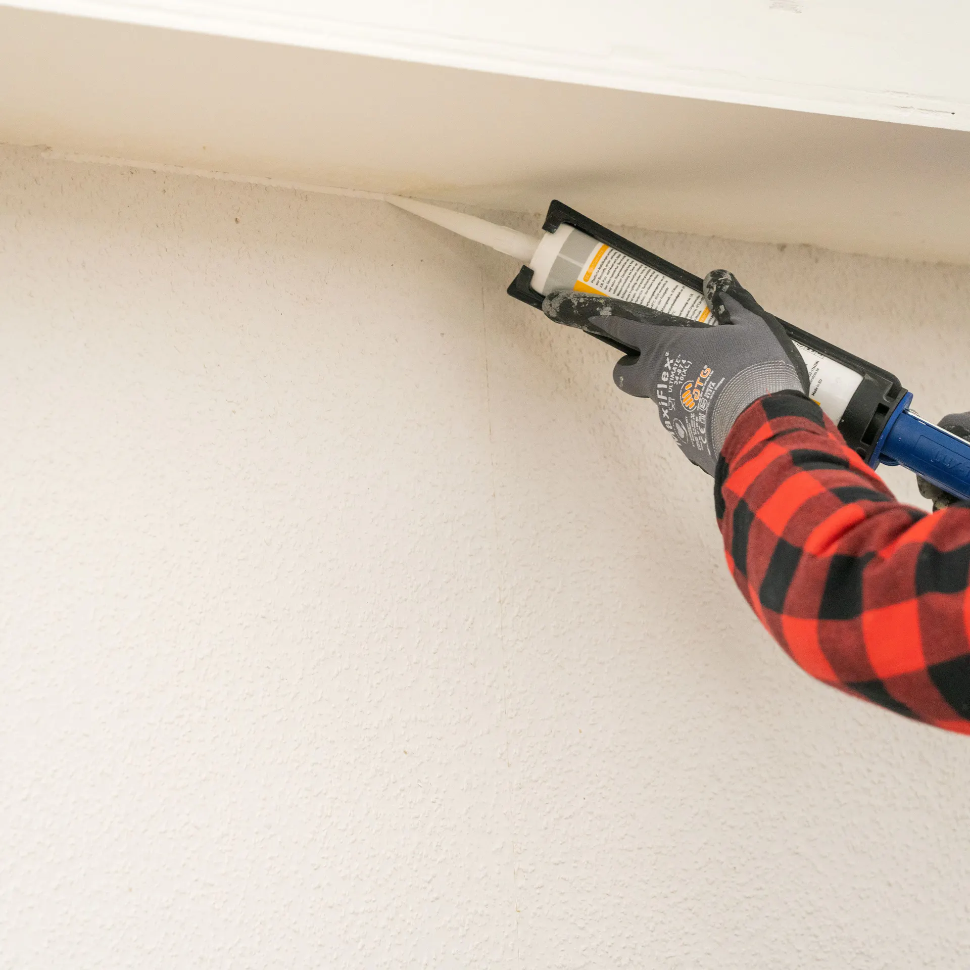 Domácí kutil aplikuje na stěnu akrylový tmel.